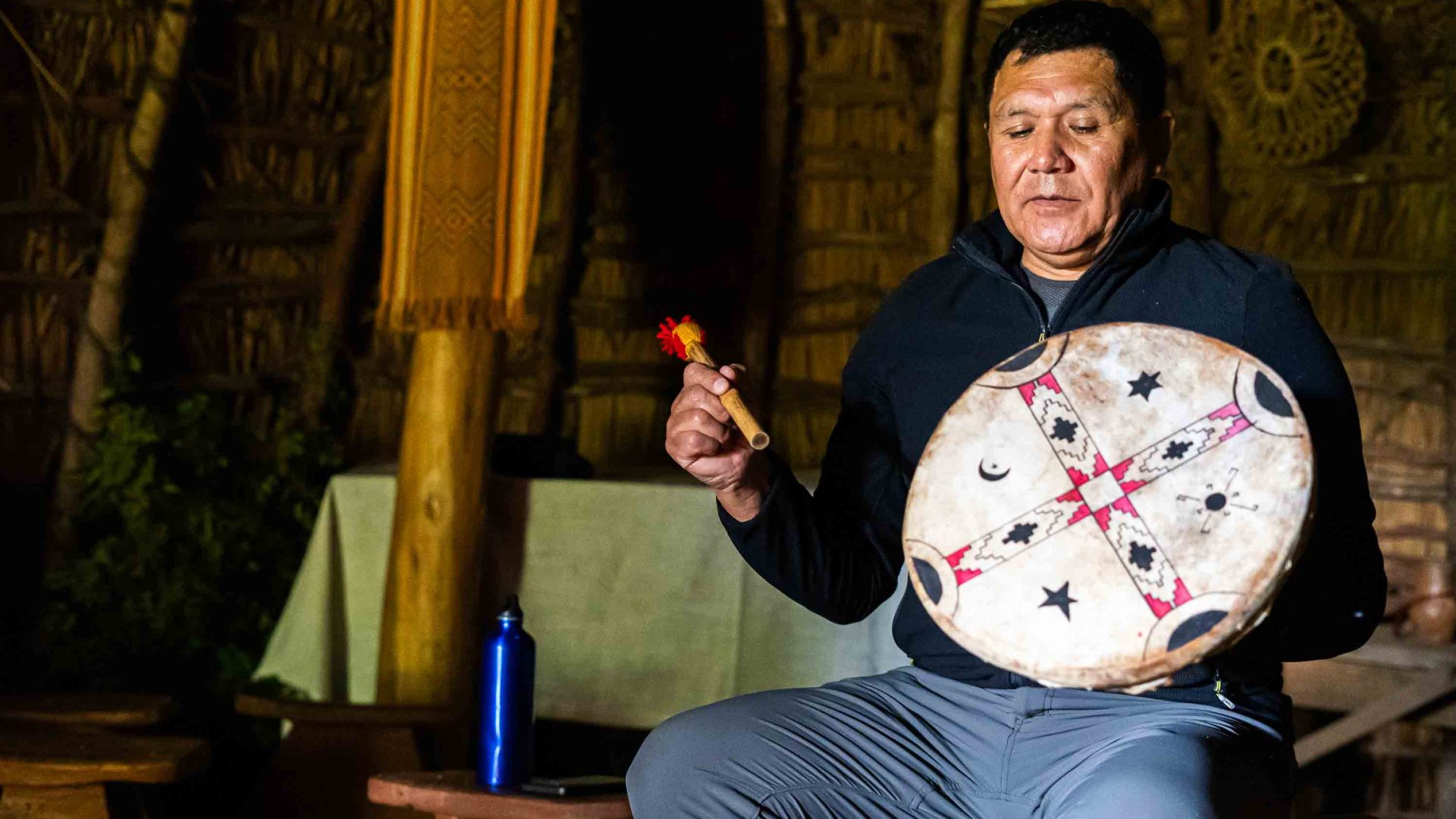 A man sits in a hut with some traditional musical instruments.