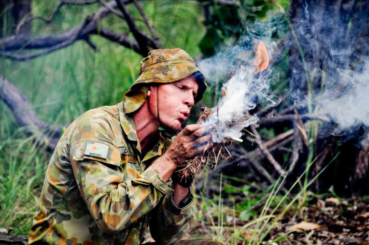 A man blows on leaves in his hands to make smoke and fire.