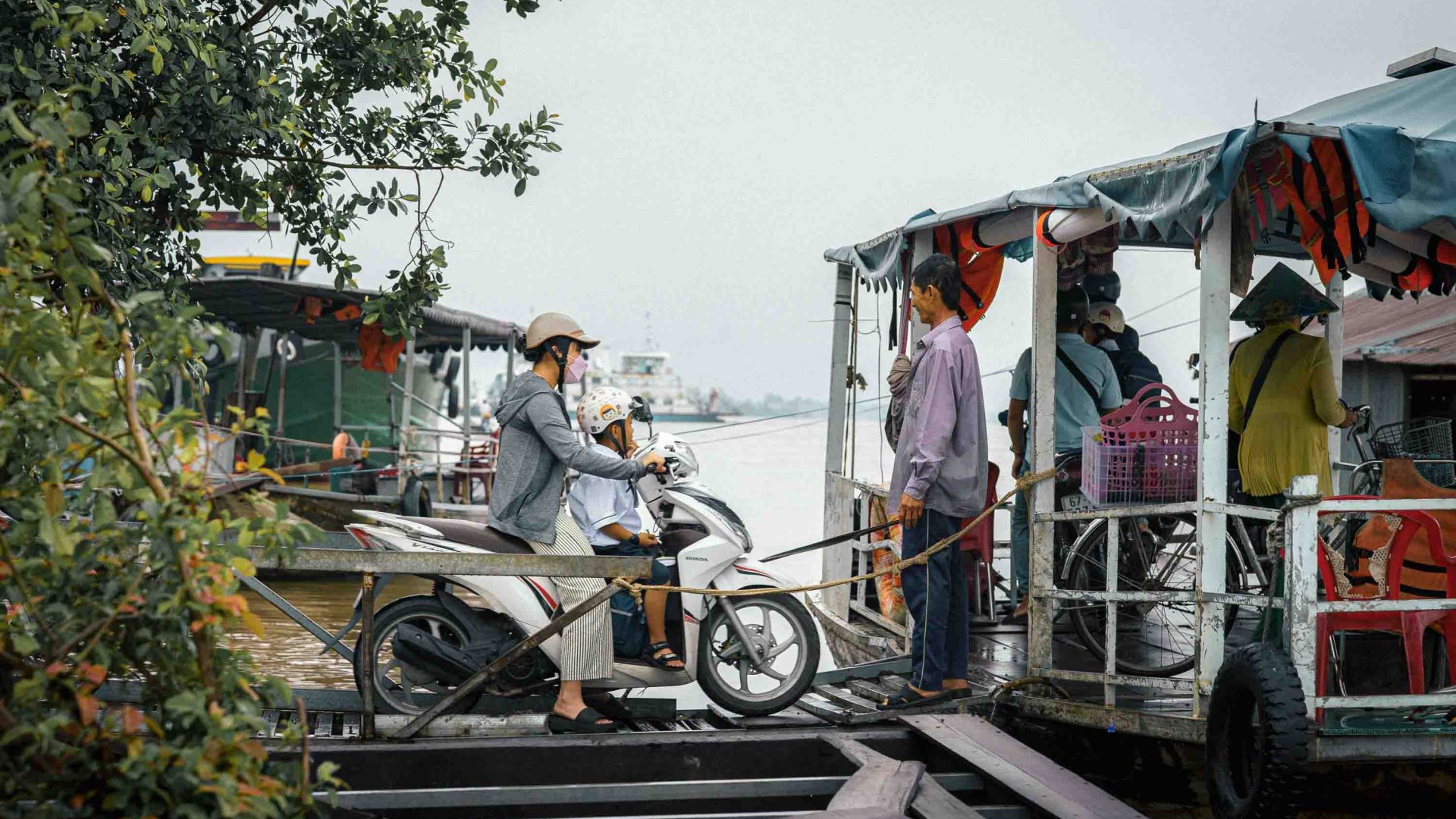 A school boy is driven on a scooter onto a boat.
