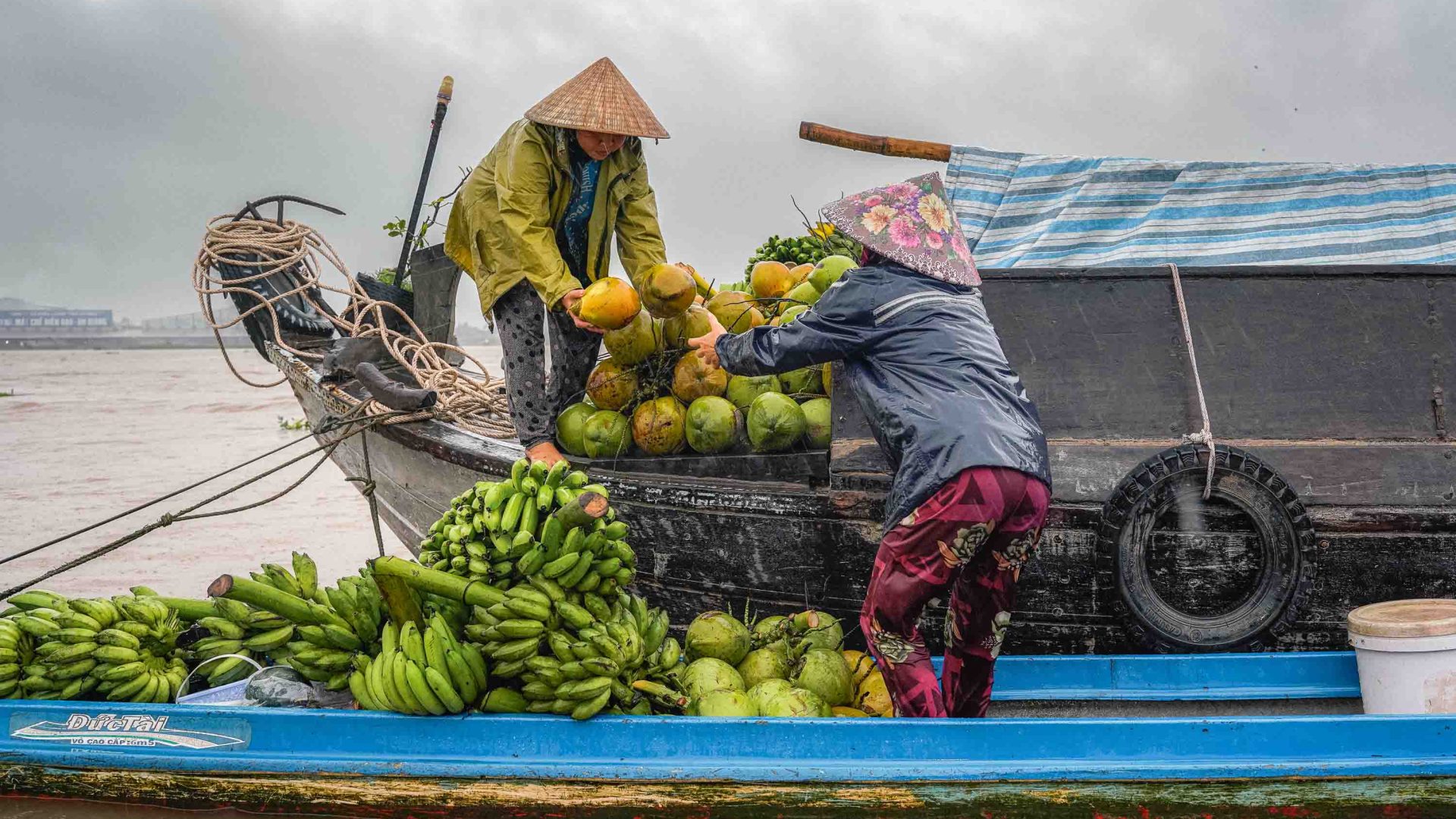 Women on boats pass bananas and coconuts.