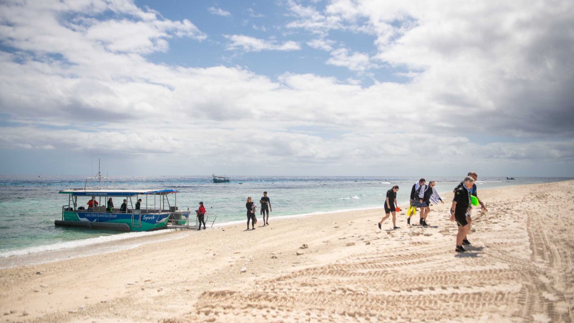 People walk up a beach away from a boat.