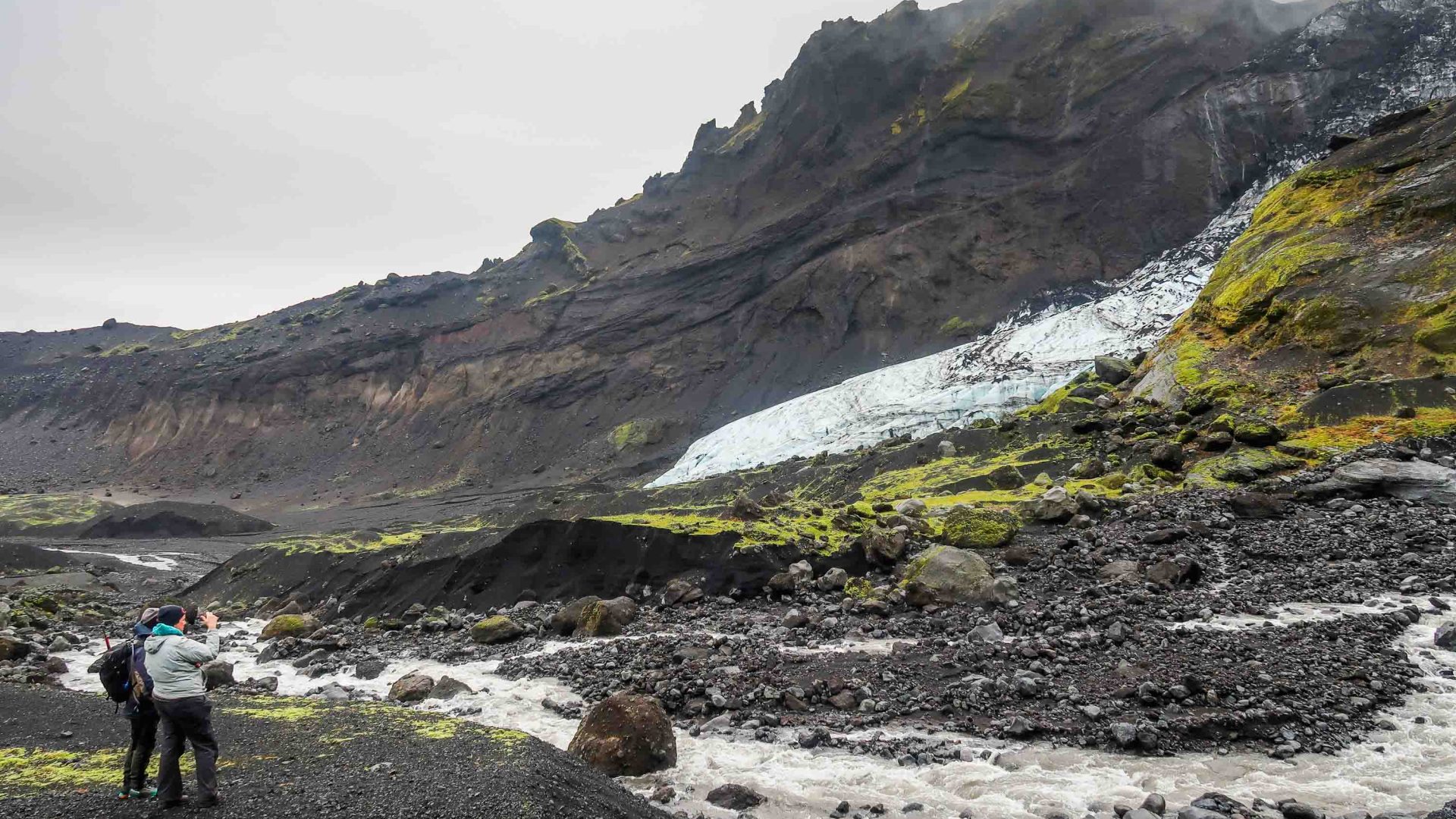 Two people stand and talk in front of a glacier.