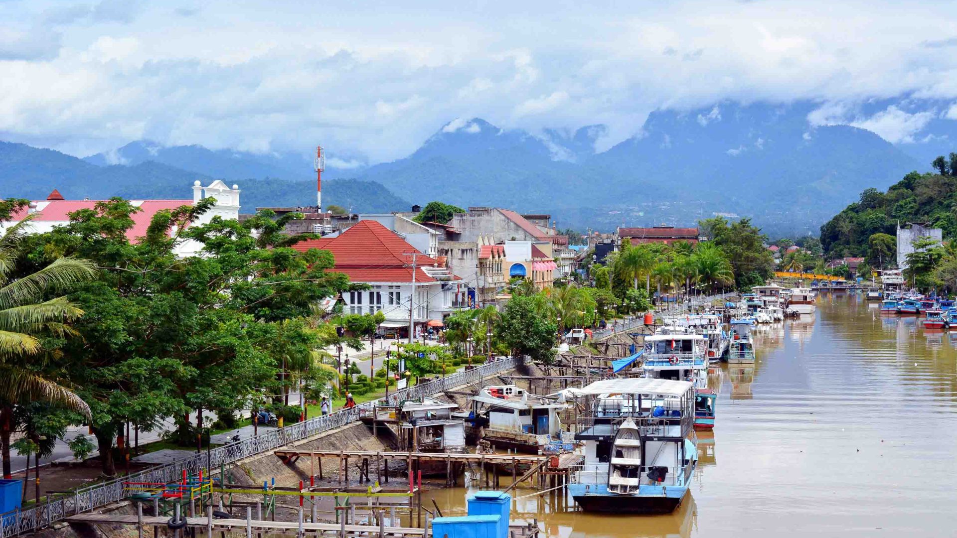 A river with boats in it alongside a town with trees and houses.