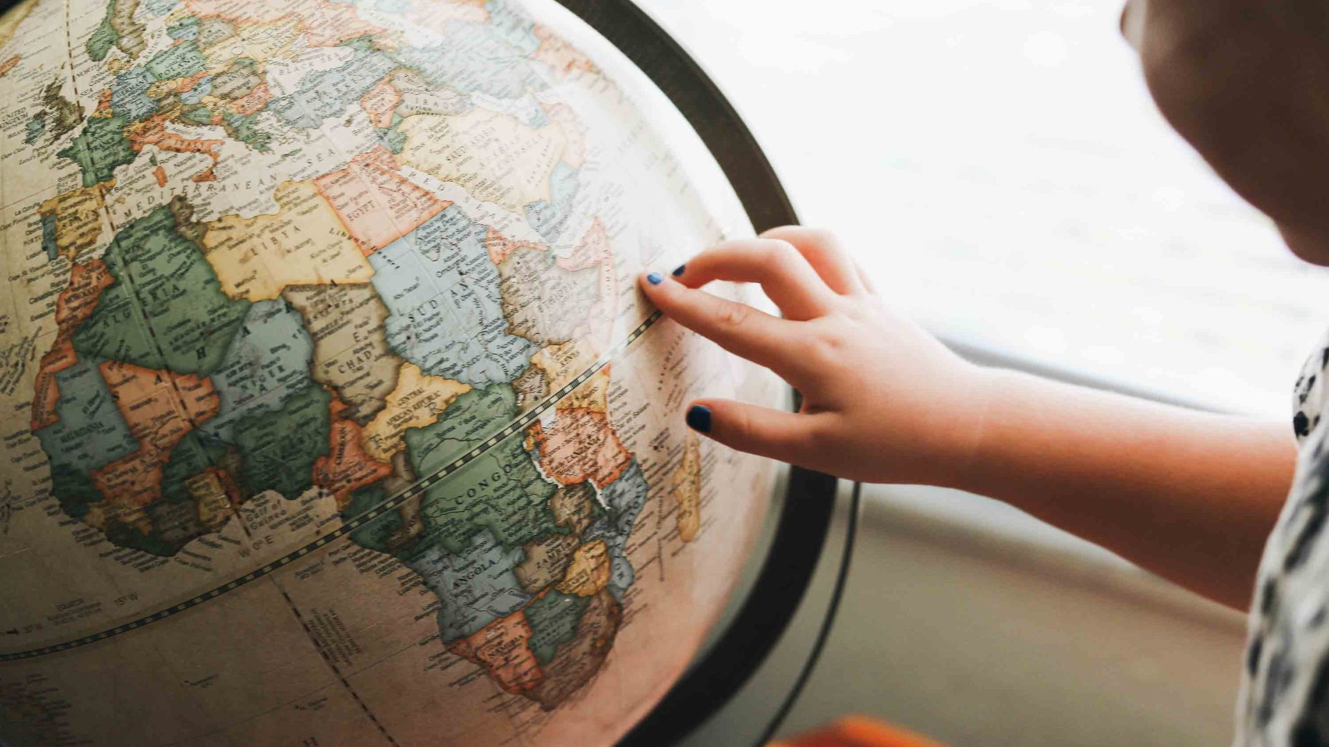 A woman points to a spot on a globe.