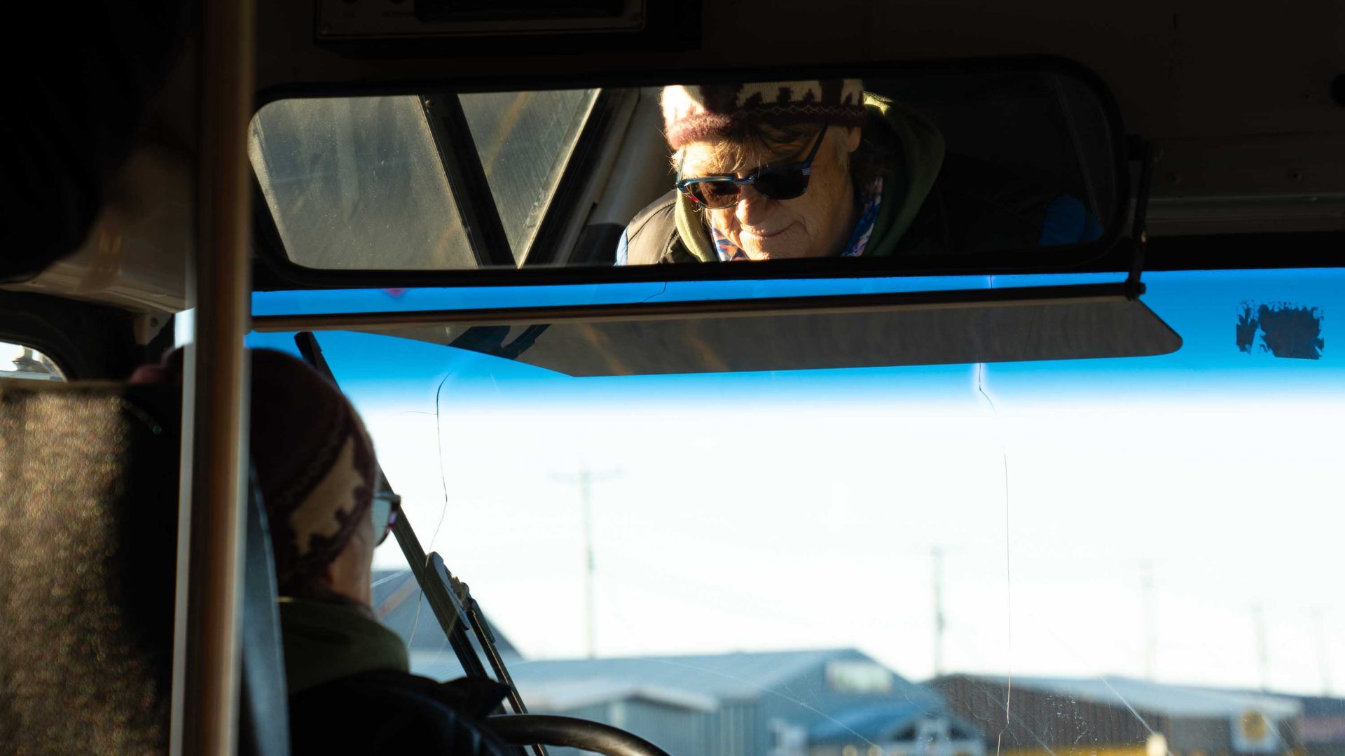 A womans face is seen in the rear view mirror of a bus she drives through town.