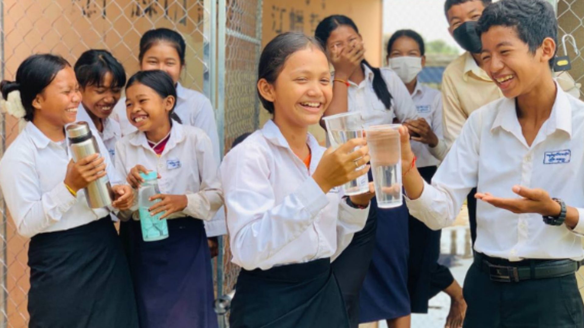 Students wearing white shirts hold glasses of clean water