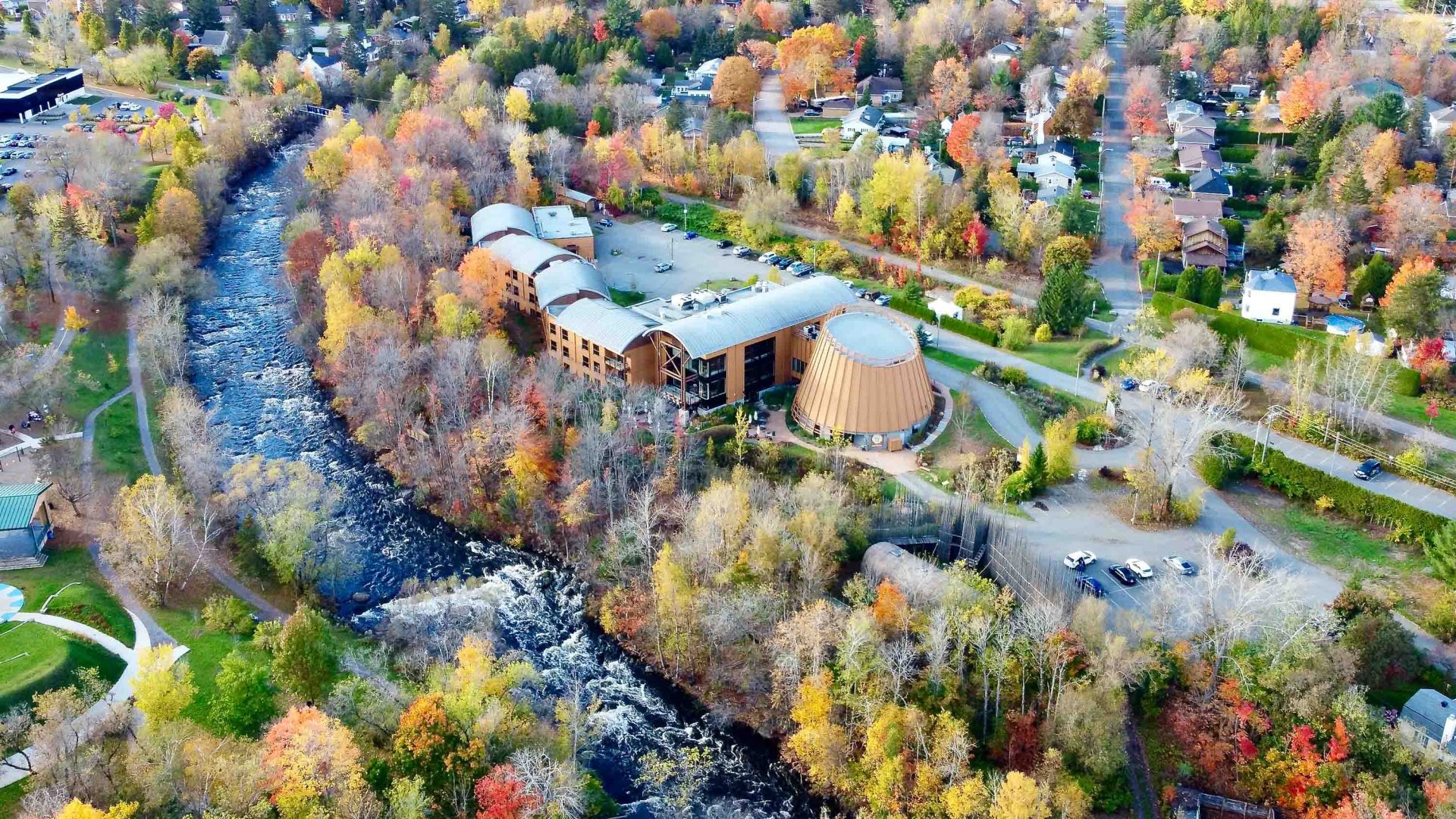 A drone photo of a hotel in amongst fall foliage, alongside a river.