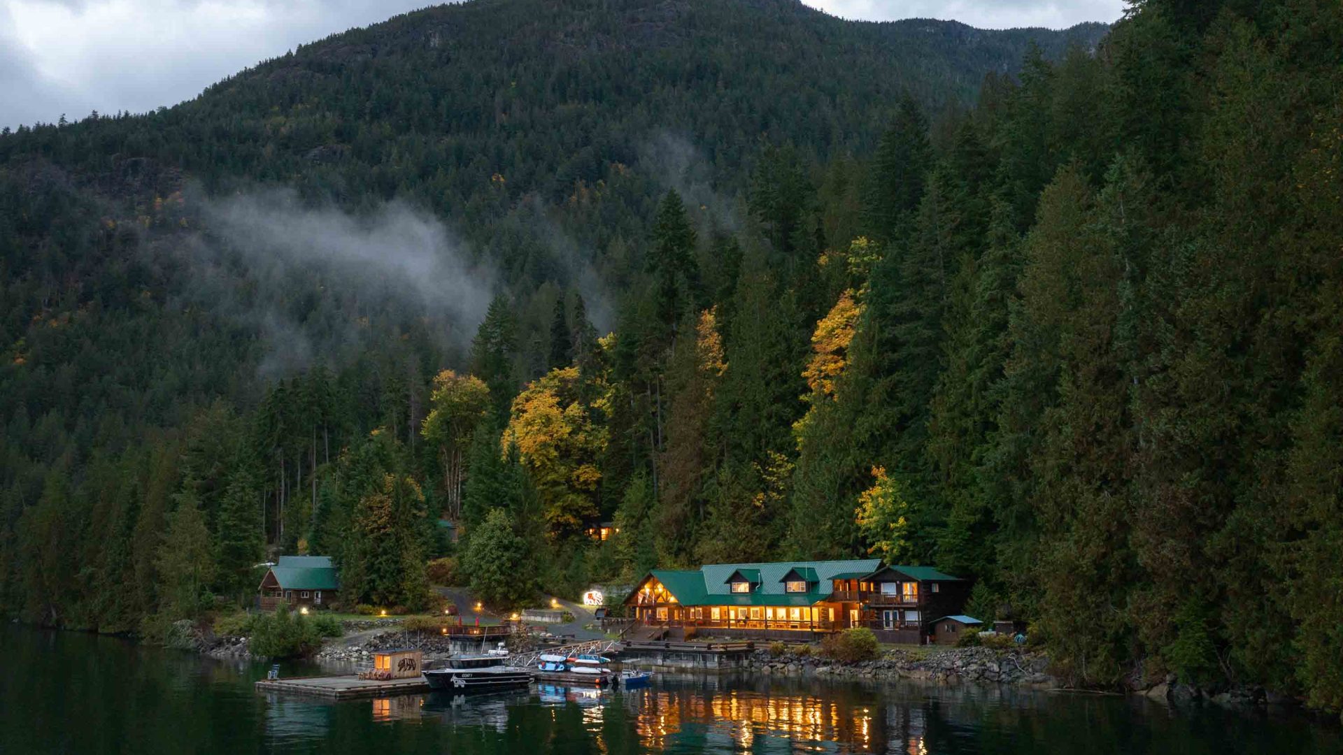 A resort by the water with verdant green forested hills behind it.