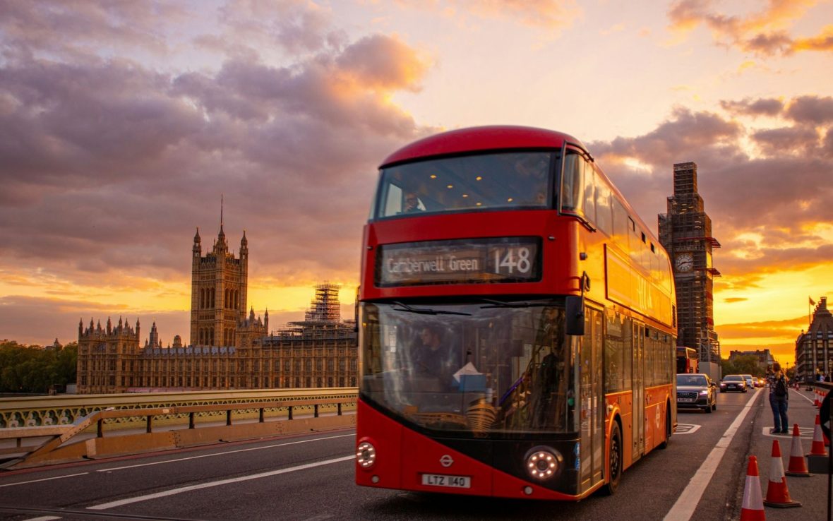 A classic red double-decker bus crosses London Bridge, with Westminster in the background.