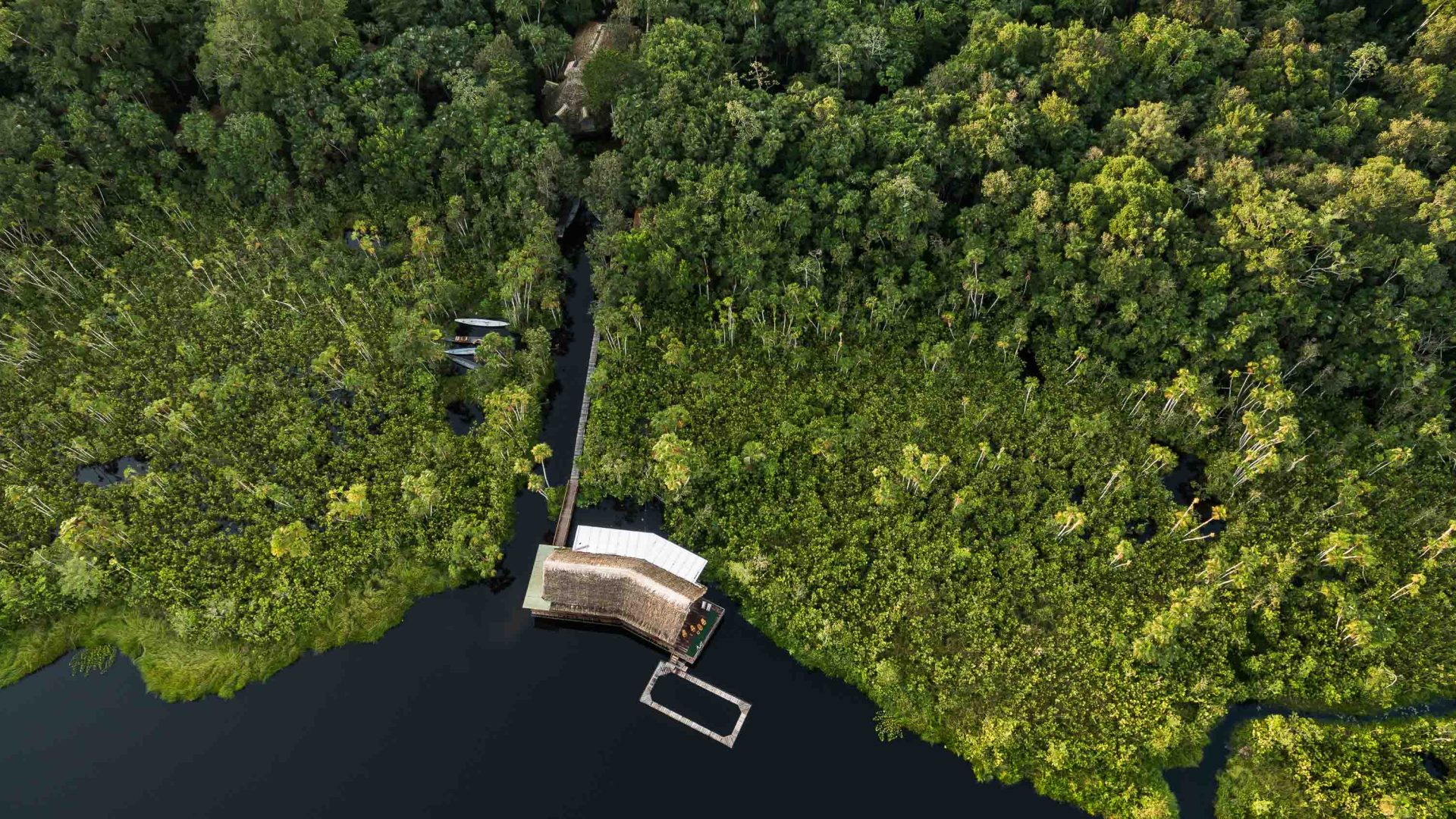 A drone shot of a lodge by some water with lots of trees around it.