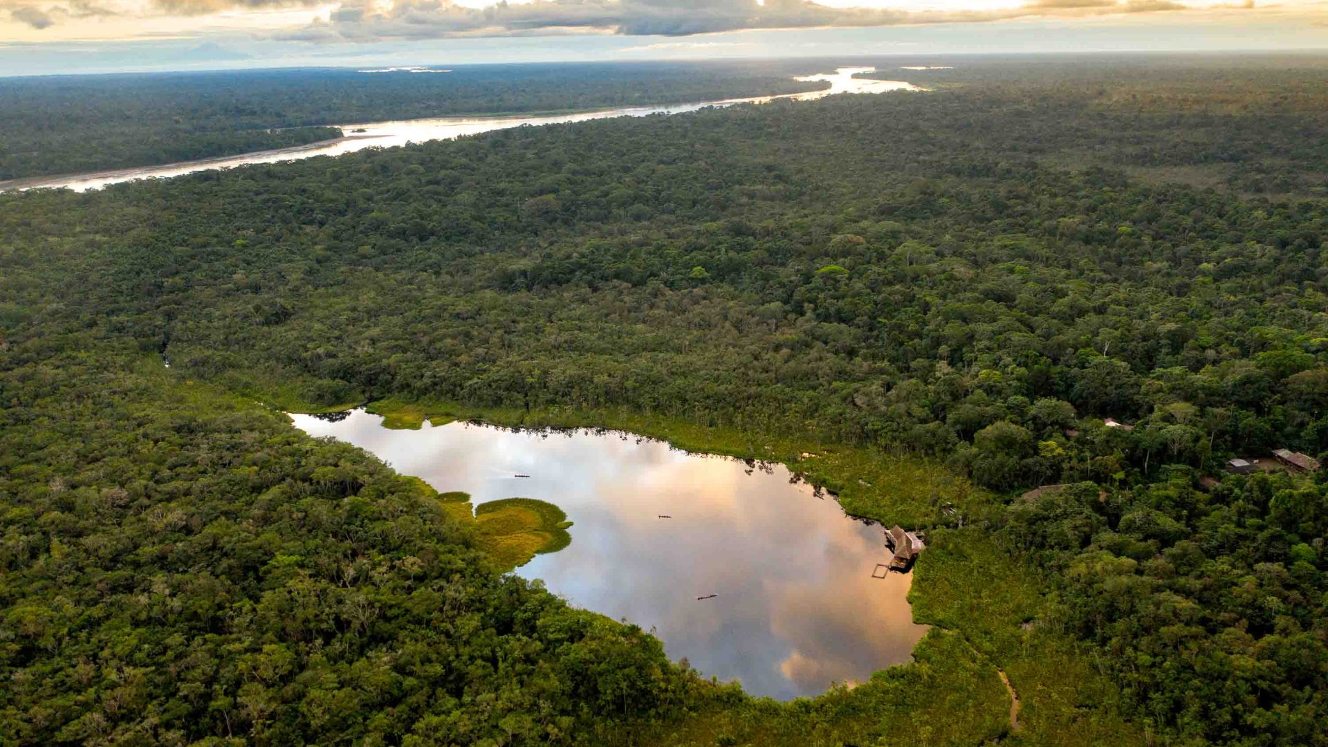 A tree filled reserve with a lake and a wooden lodge nestled to one side of it.