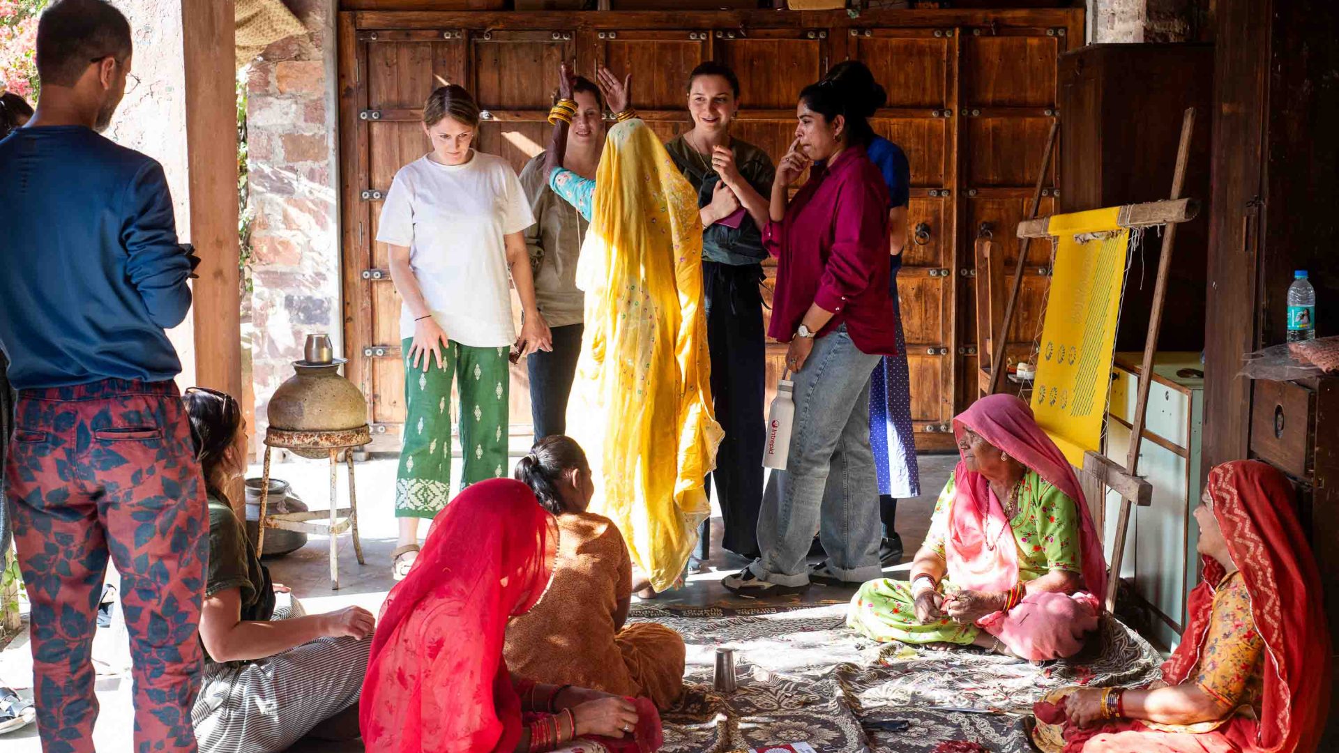 A group of travelers stands and sits amongst artisans hard at work.