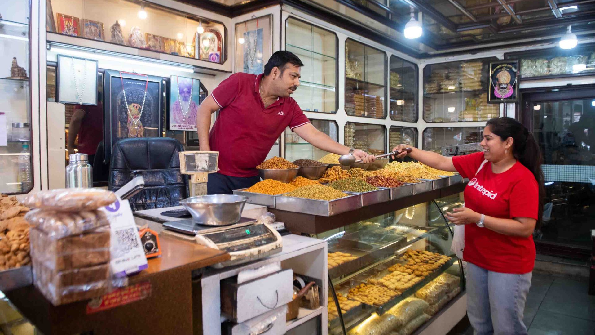 A female tour guide in a red t-shirt buys sweets from a male vendor.