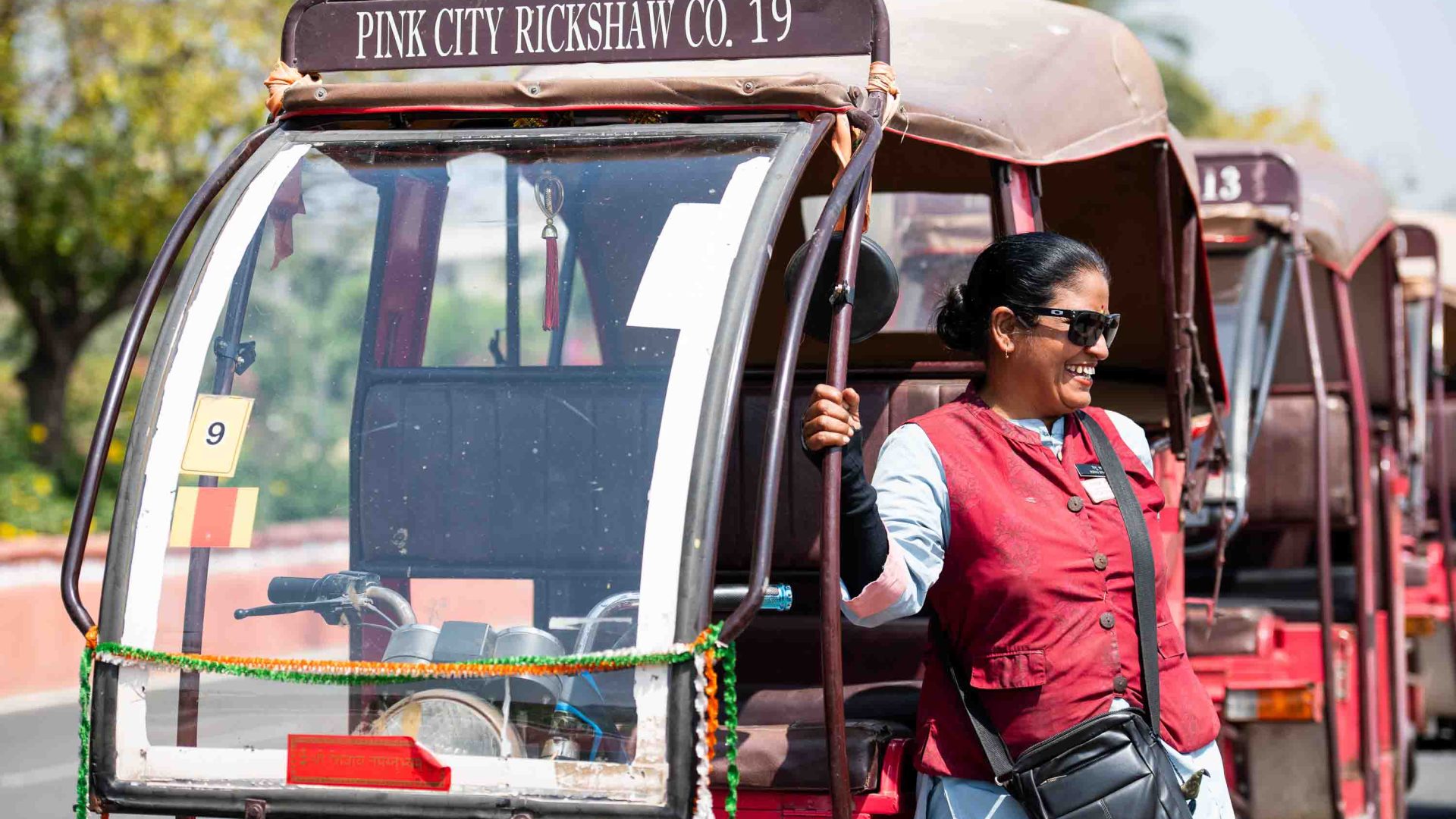 A woman smiles alongside her rickshaw.