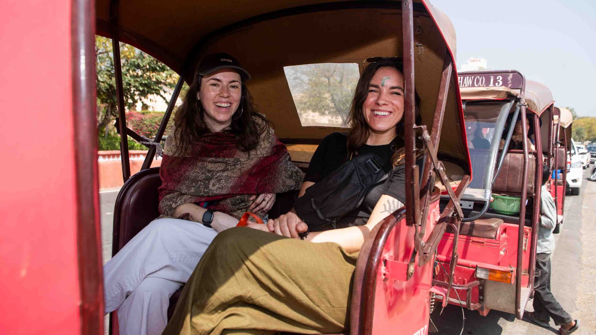 Two women sit in the back of a rickshaw.