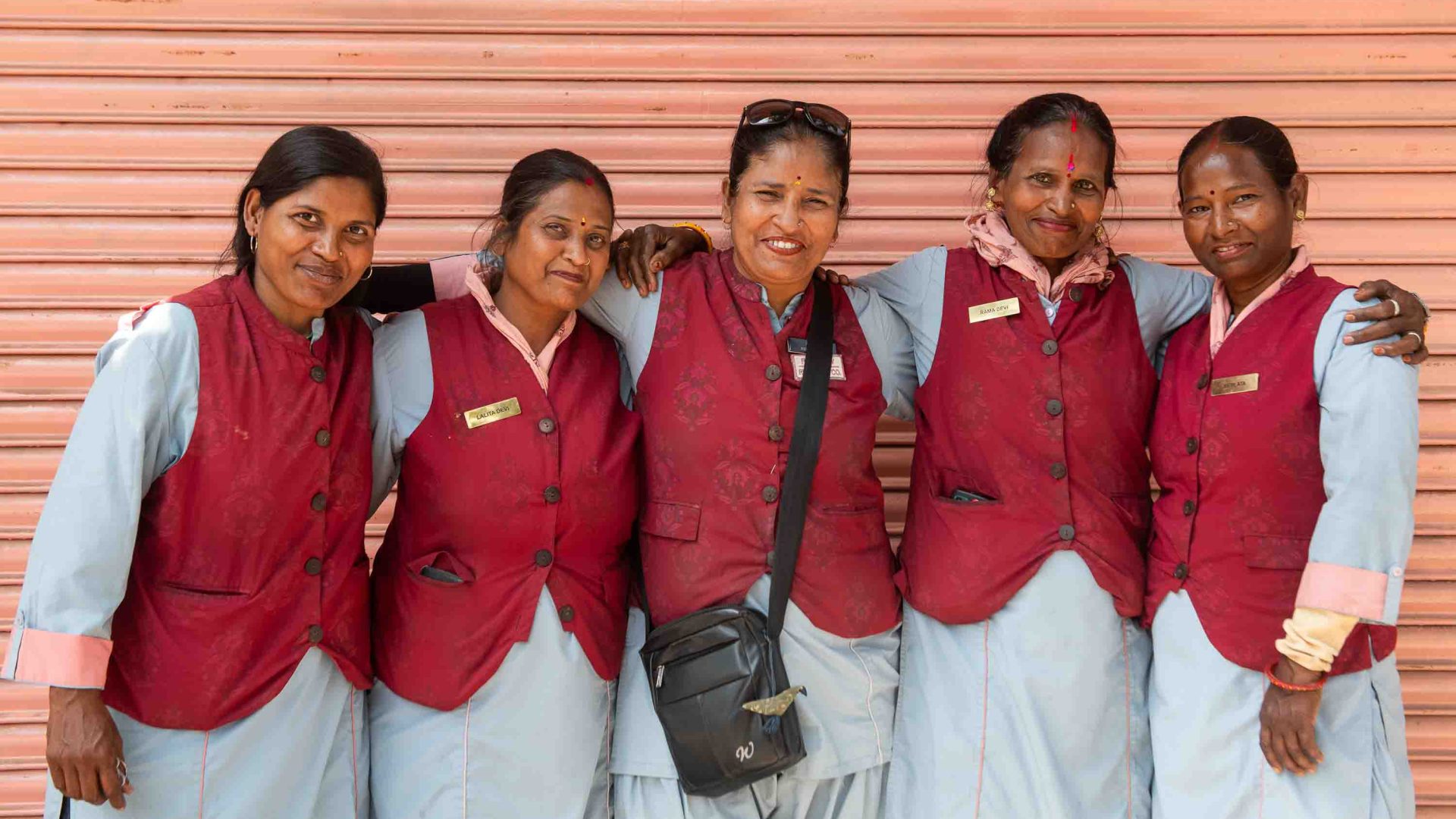 A group of female rickshaw drivers in uniforms have their arms over each others shoulders in a group photo.