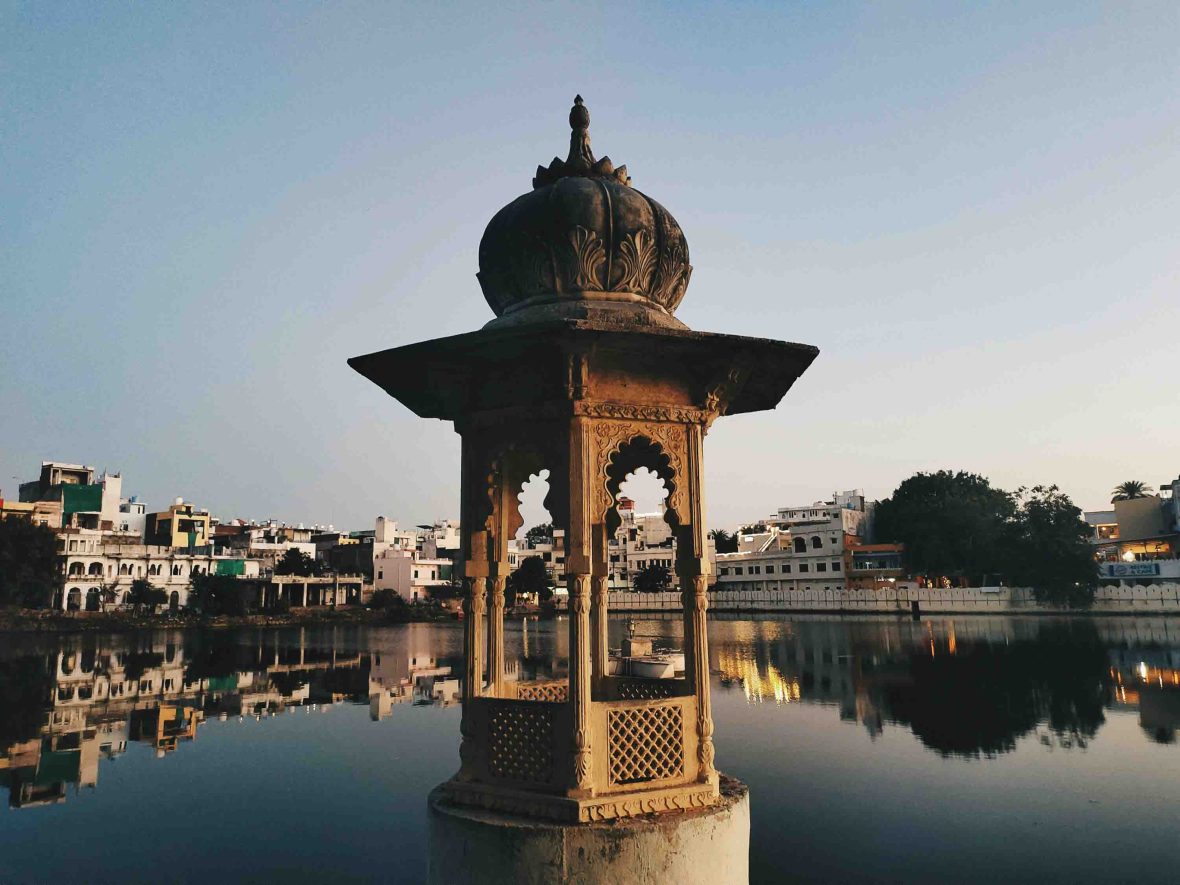 A stone structure in front of a lake with buildings on the other side.