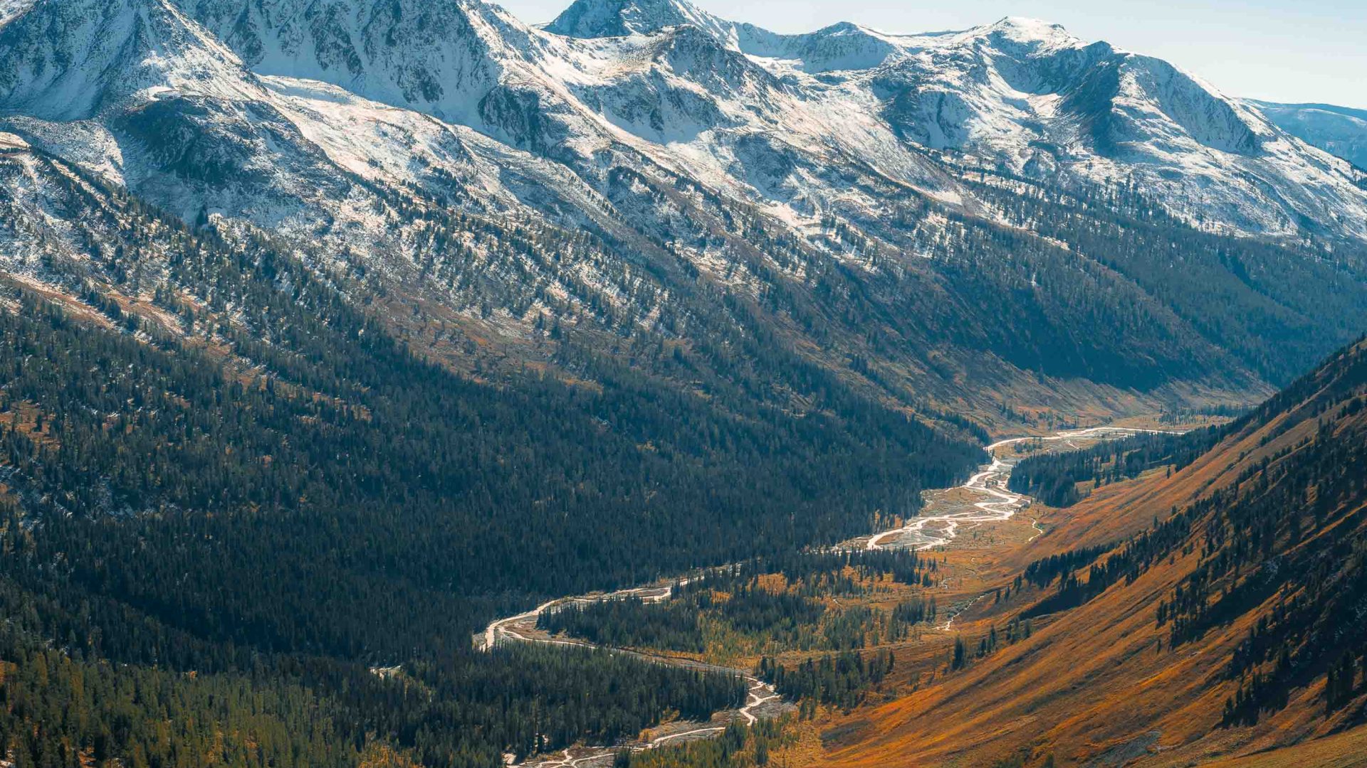 A river through a valley lined with snowy mountains.