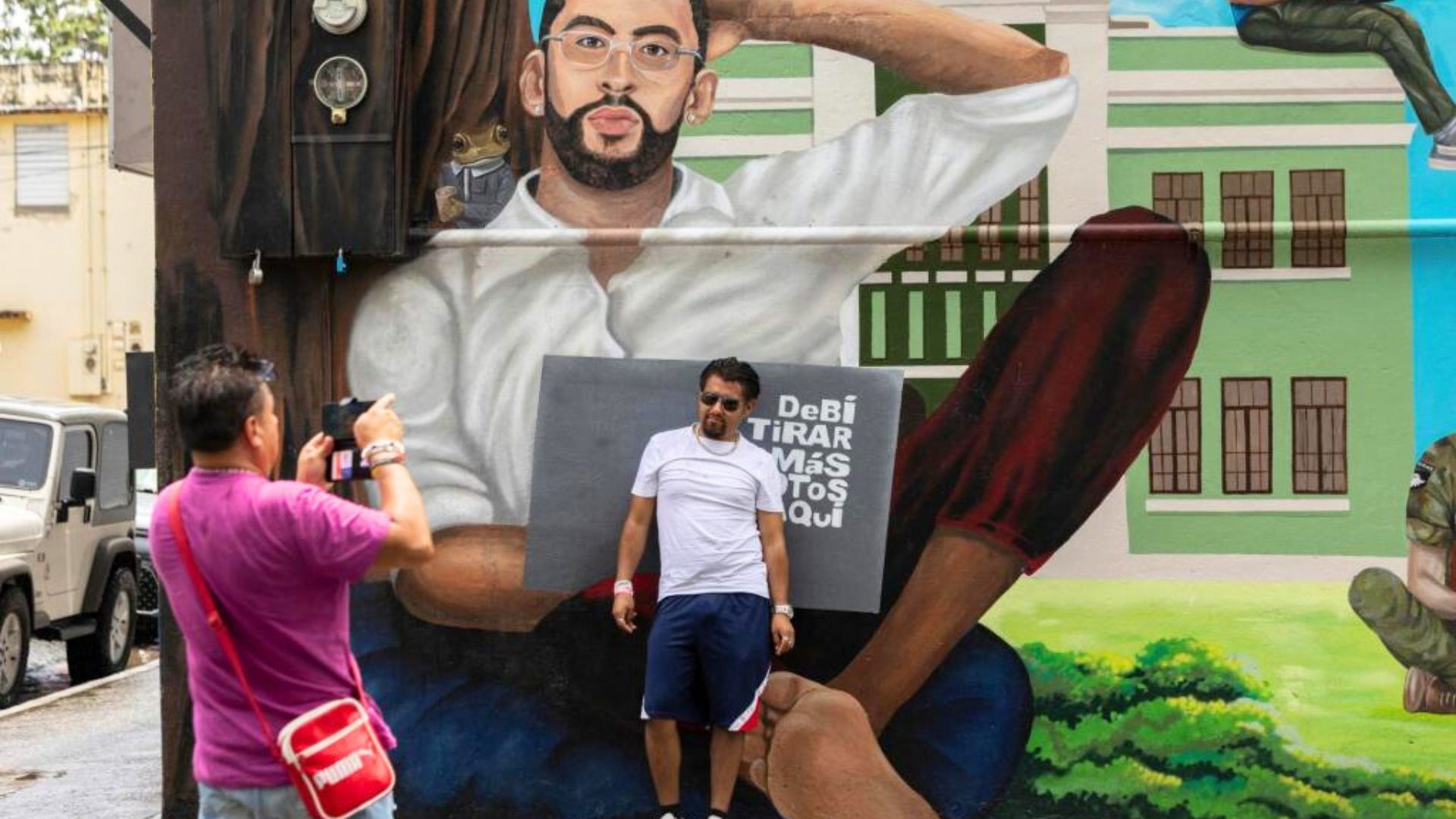 Two people take a photo in front of mural of Bad Bunny, the musician.
