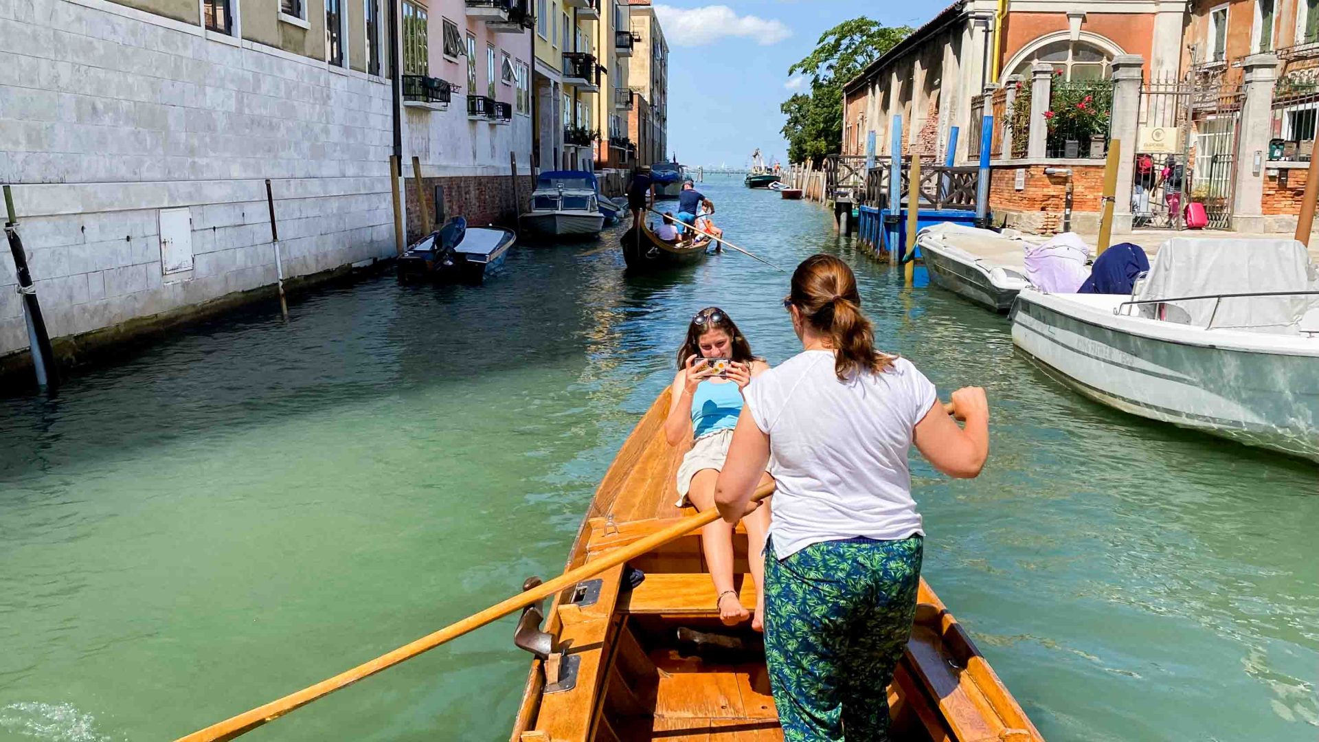 Two women row a boat in a canal.