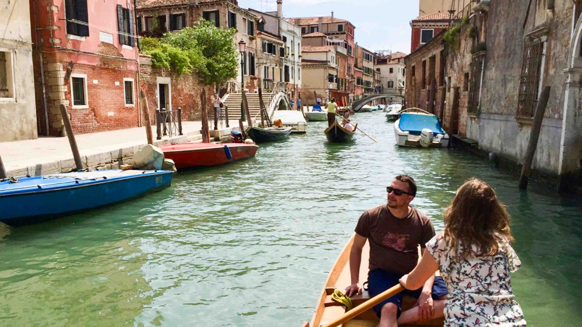 A woman rows a man down a canal.
