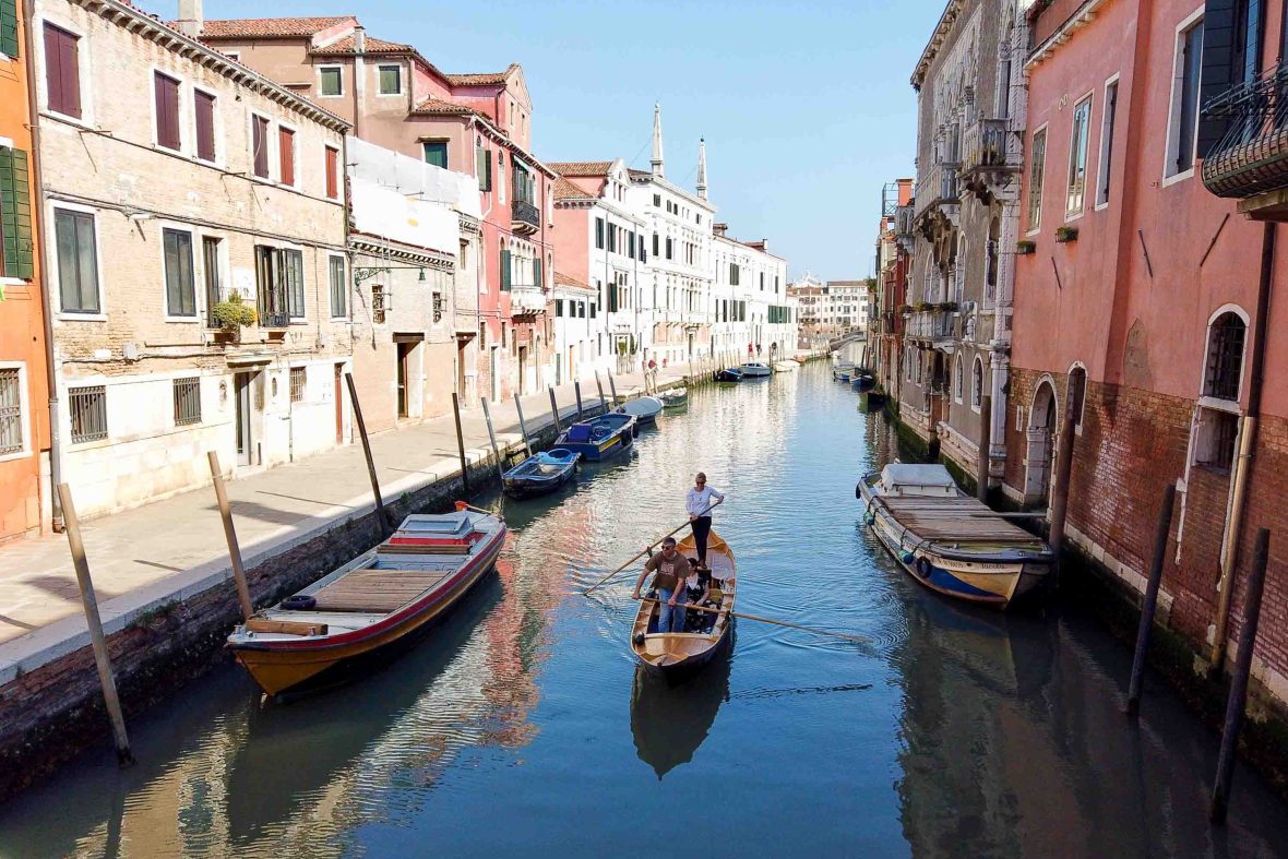 A woman stands and rows in a canal in Venice.