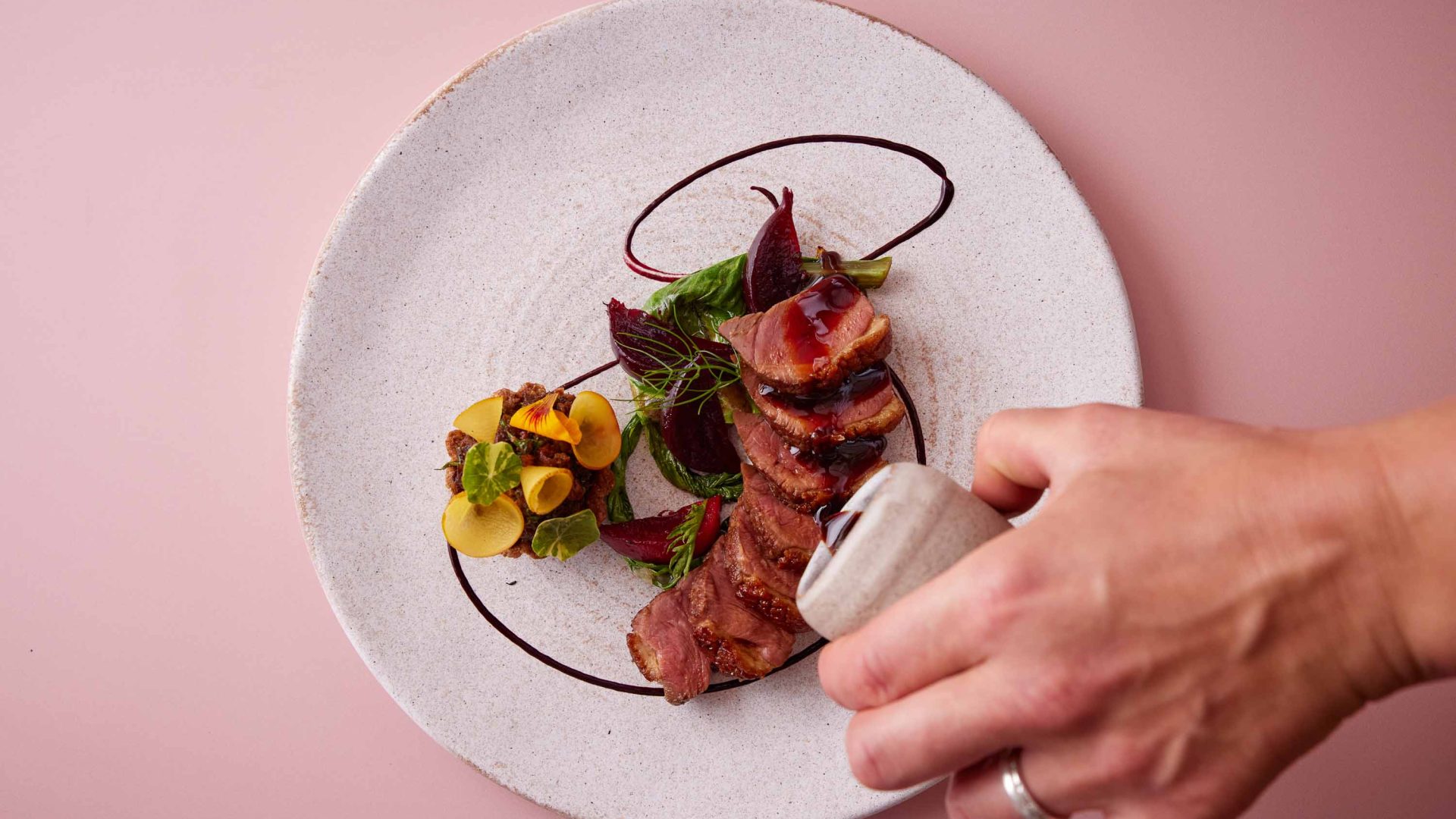 A hand tips salt onto a dish of duck with vegetables.