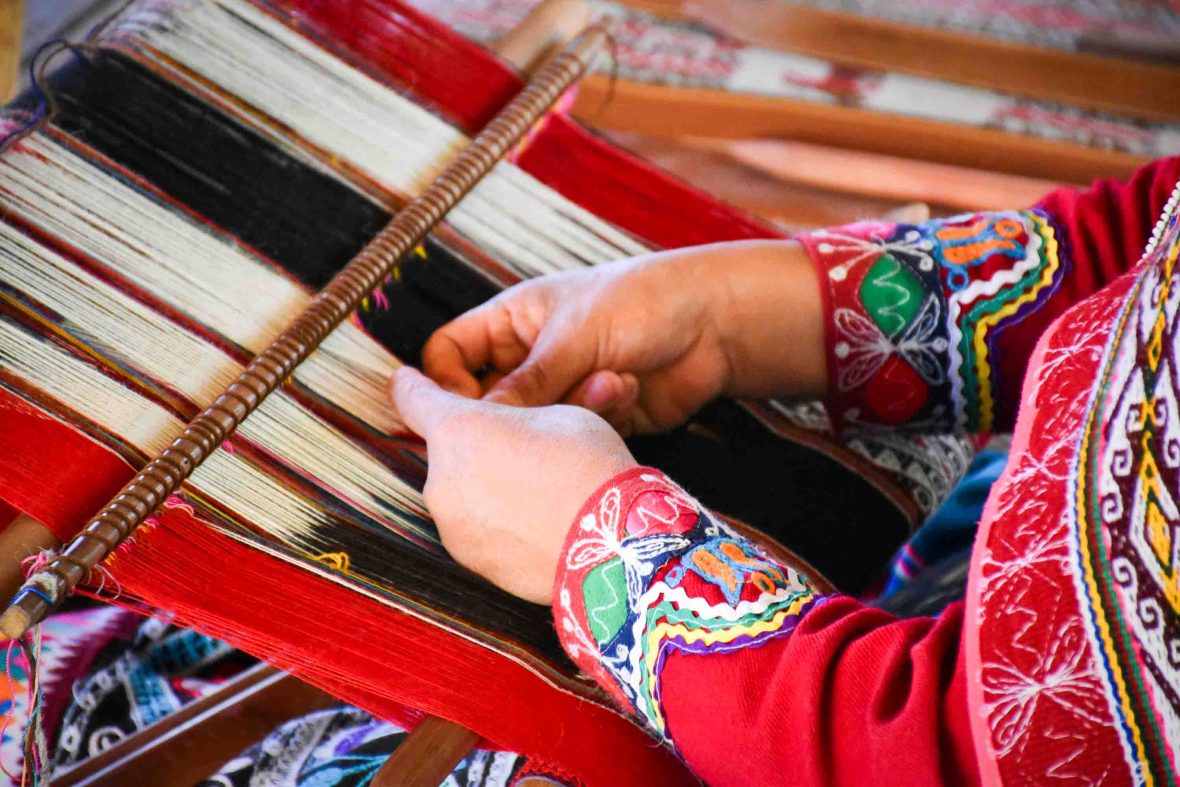 Hands in a red outfit weave using red and white yarn.