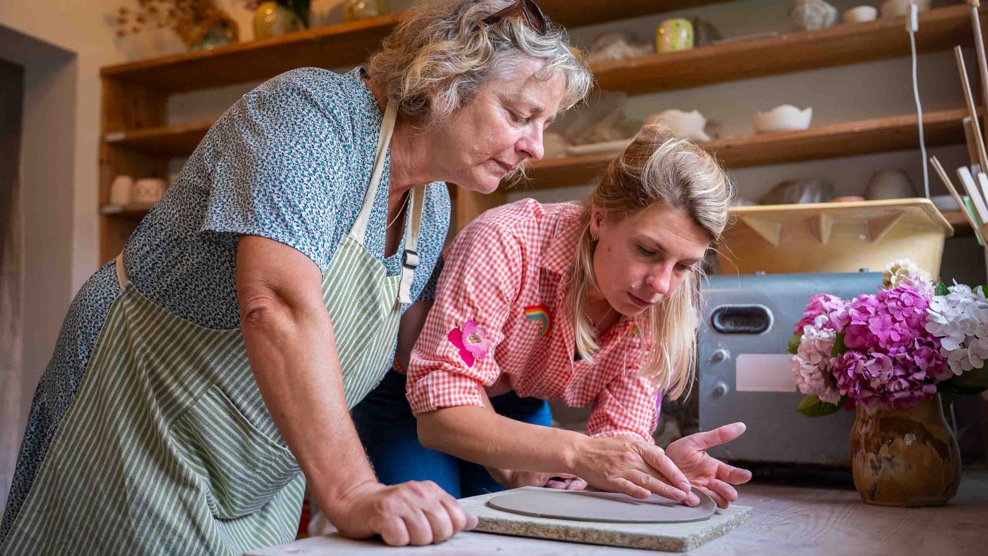 Two women carefully lift some clay from a tray.