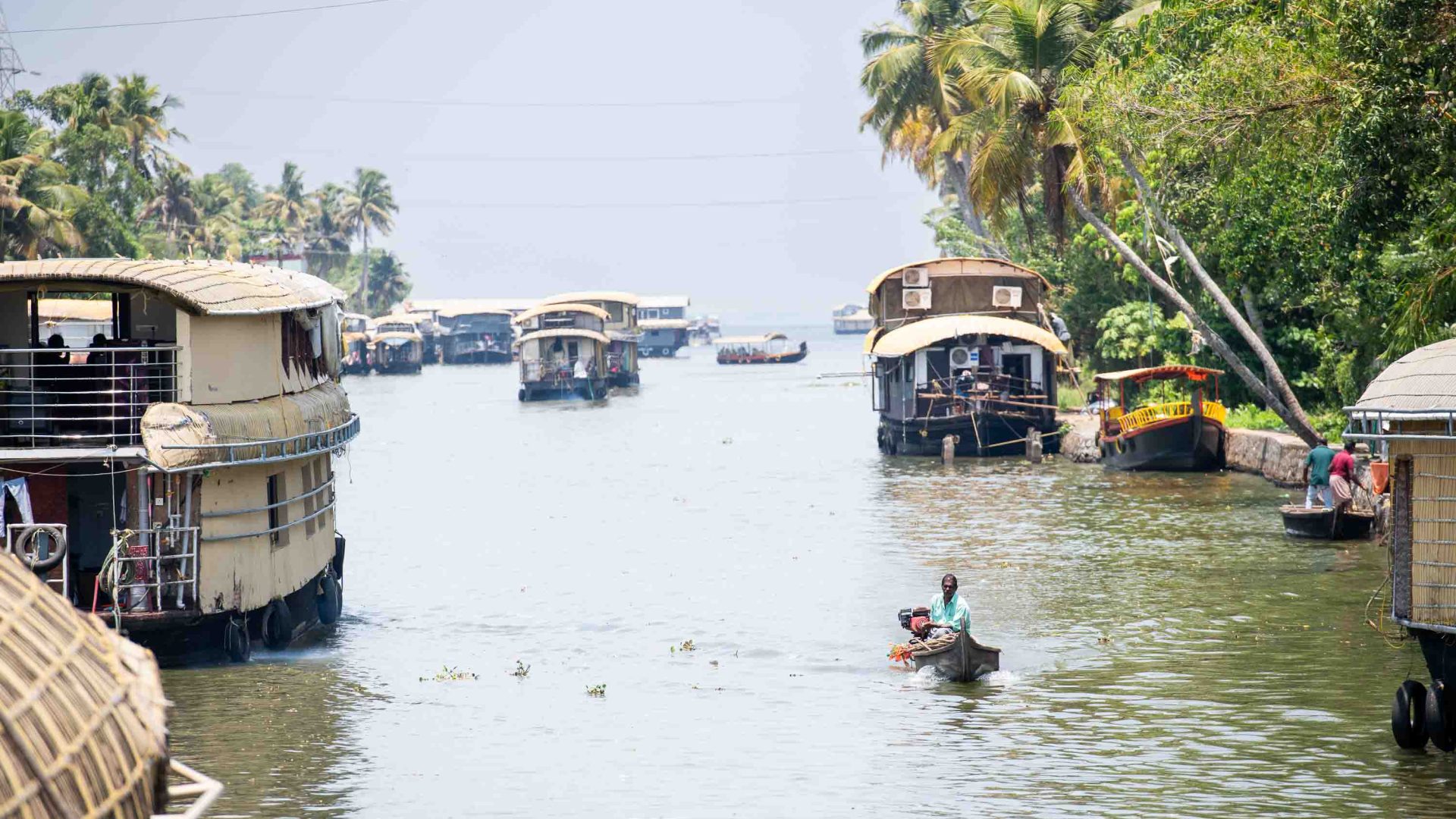 A small boat moves through waterways, flanked by larger houseboats.