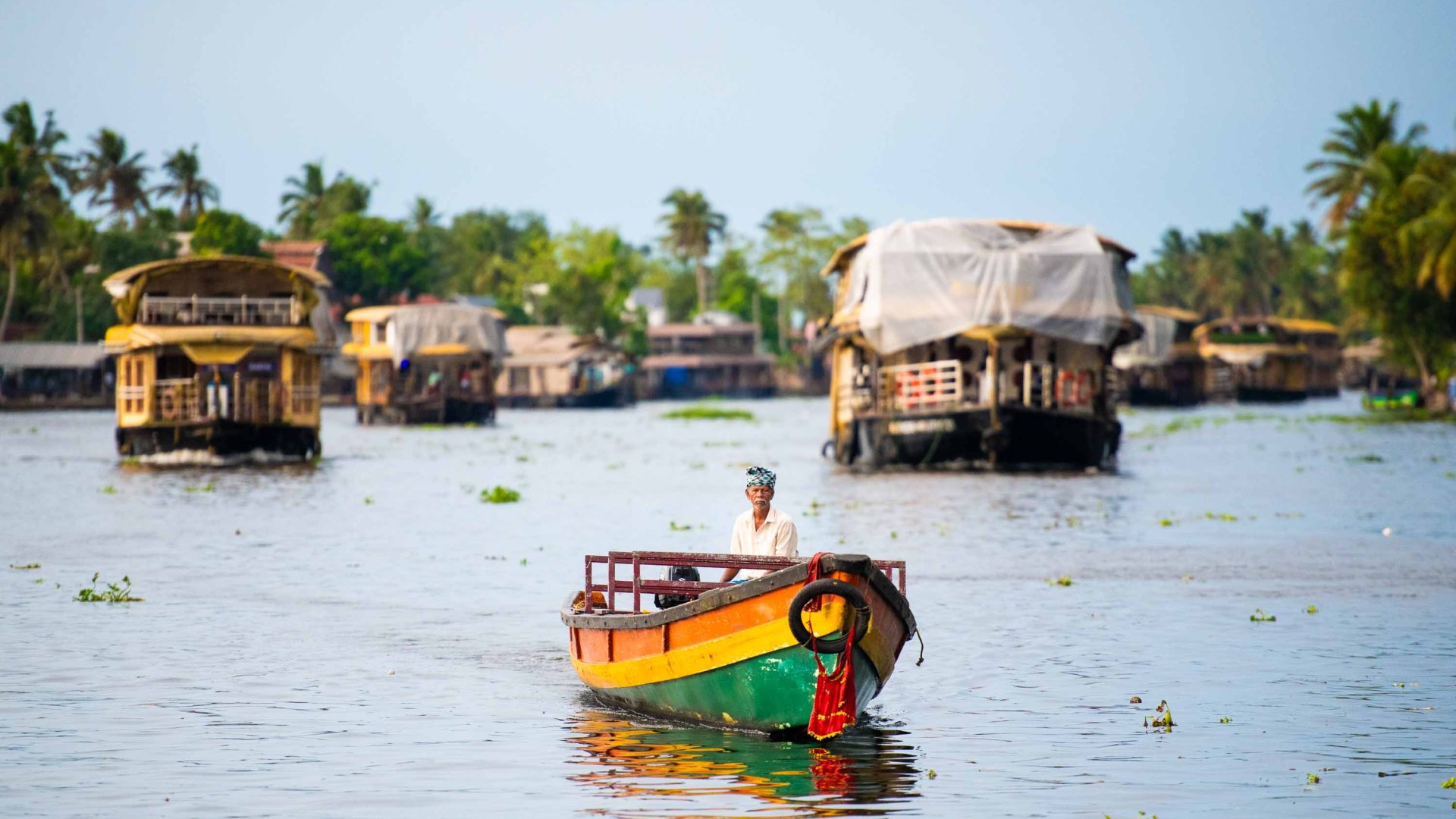 A small boat moves through waterways, flanked by larger houseboats.