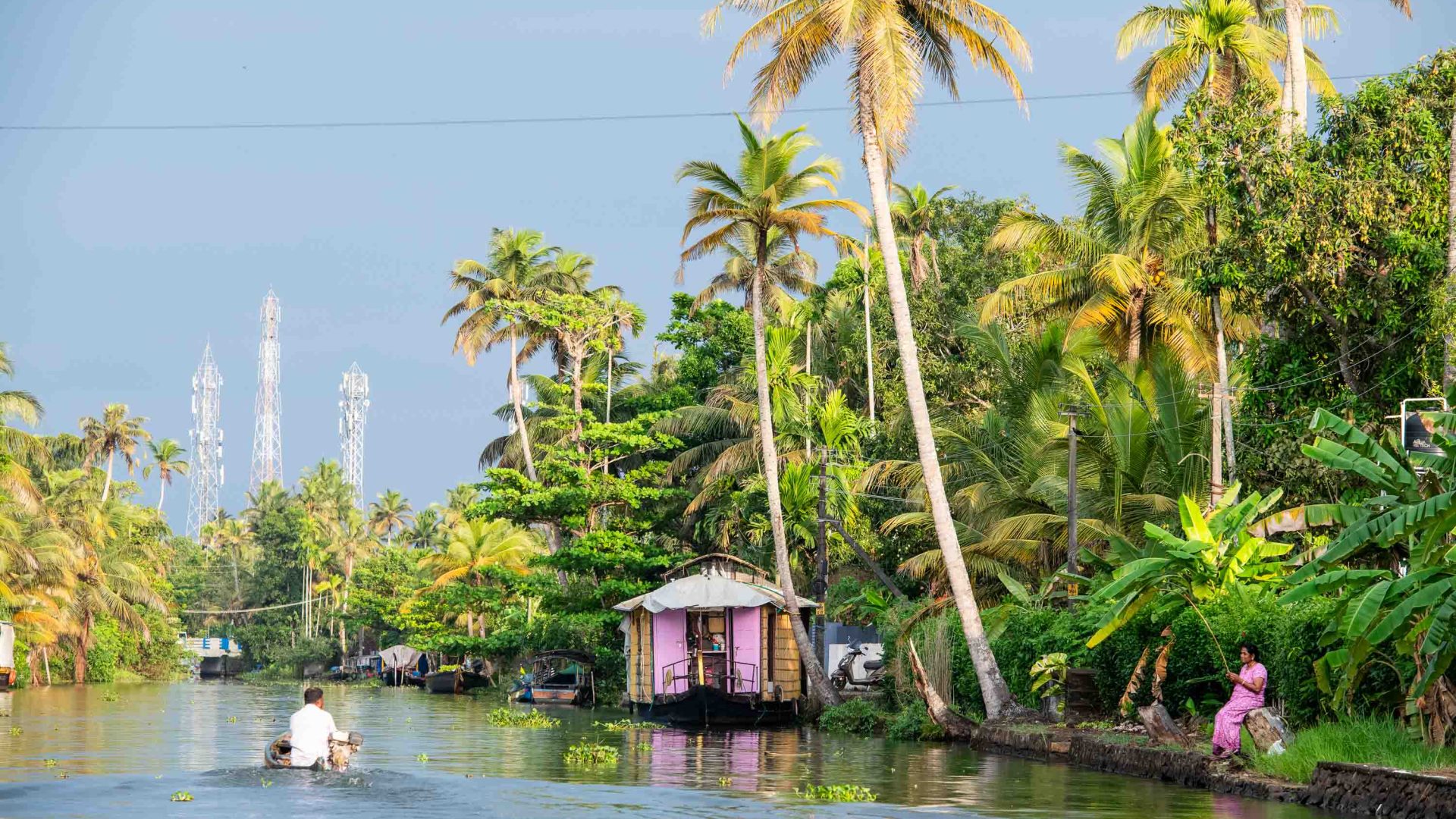 A small boat glides past a pink house and palm trees.