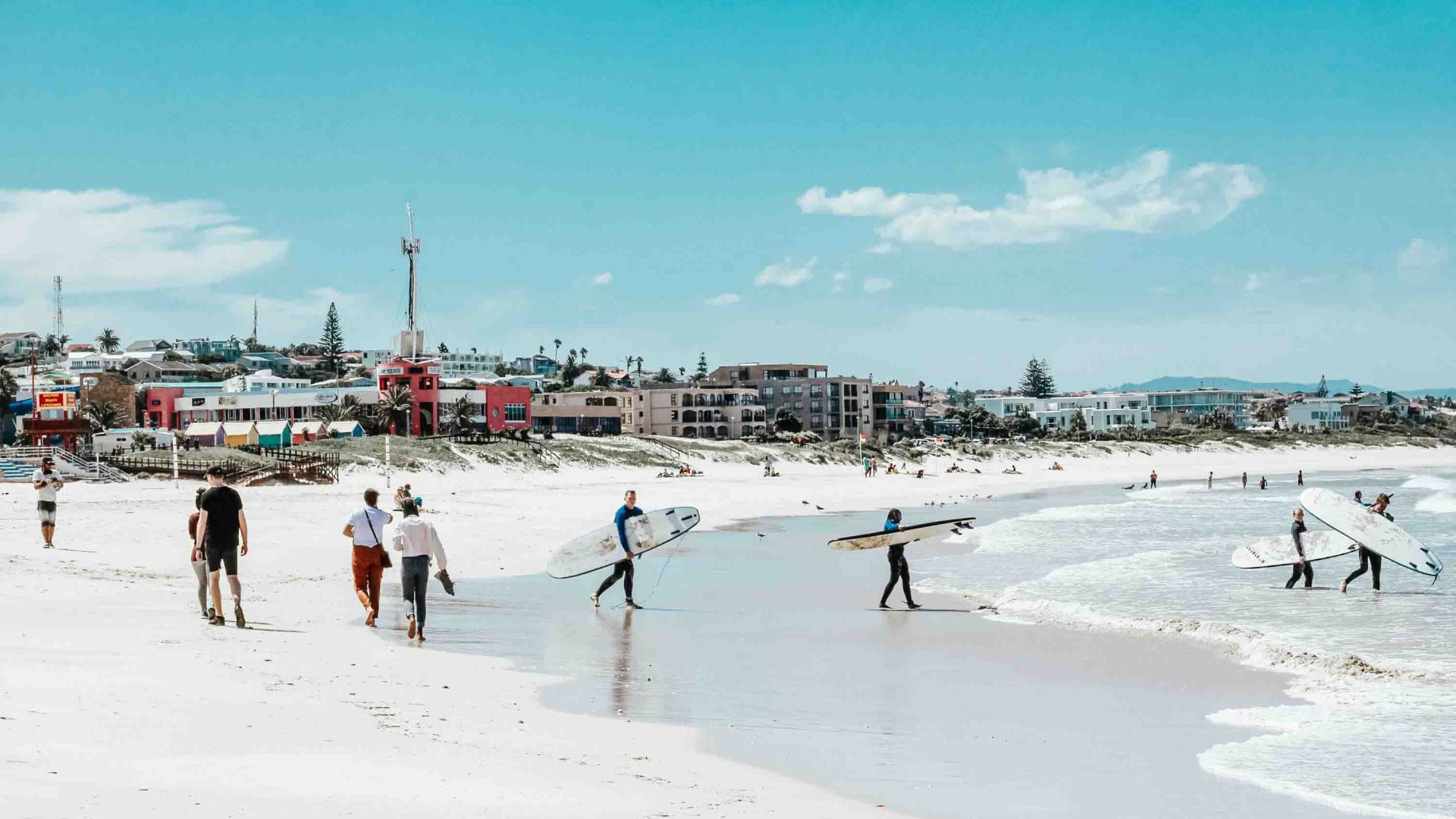 Surfers on a beach that has buildings fronting it.