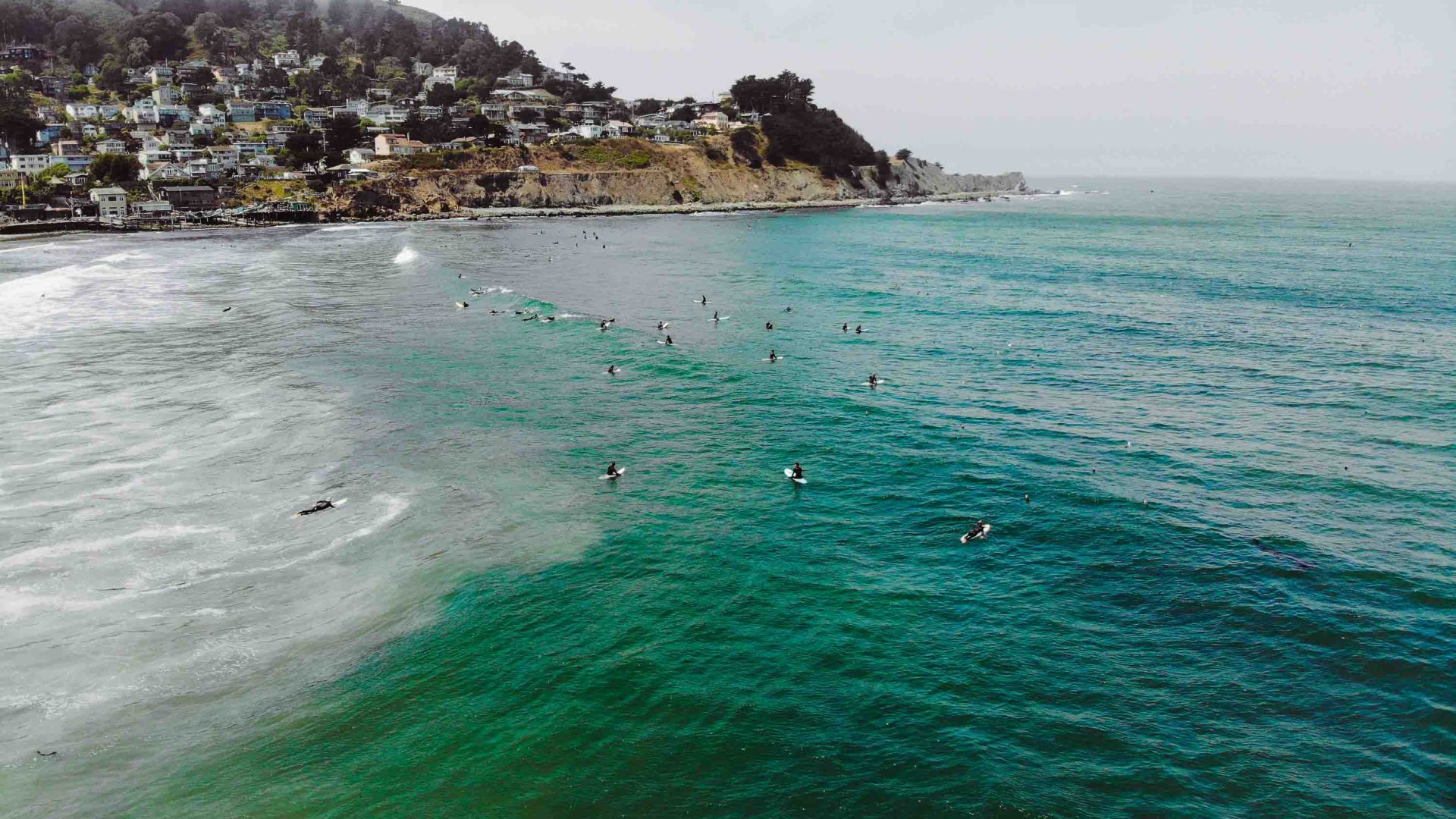 A drone photo of coastline and surfers in the sea.