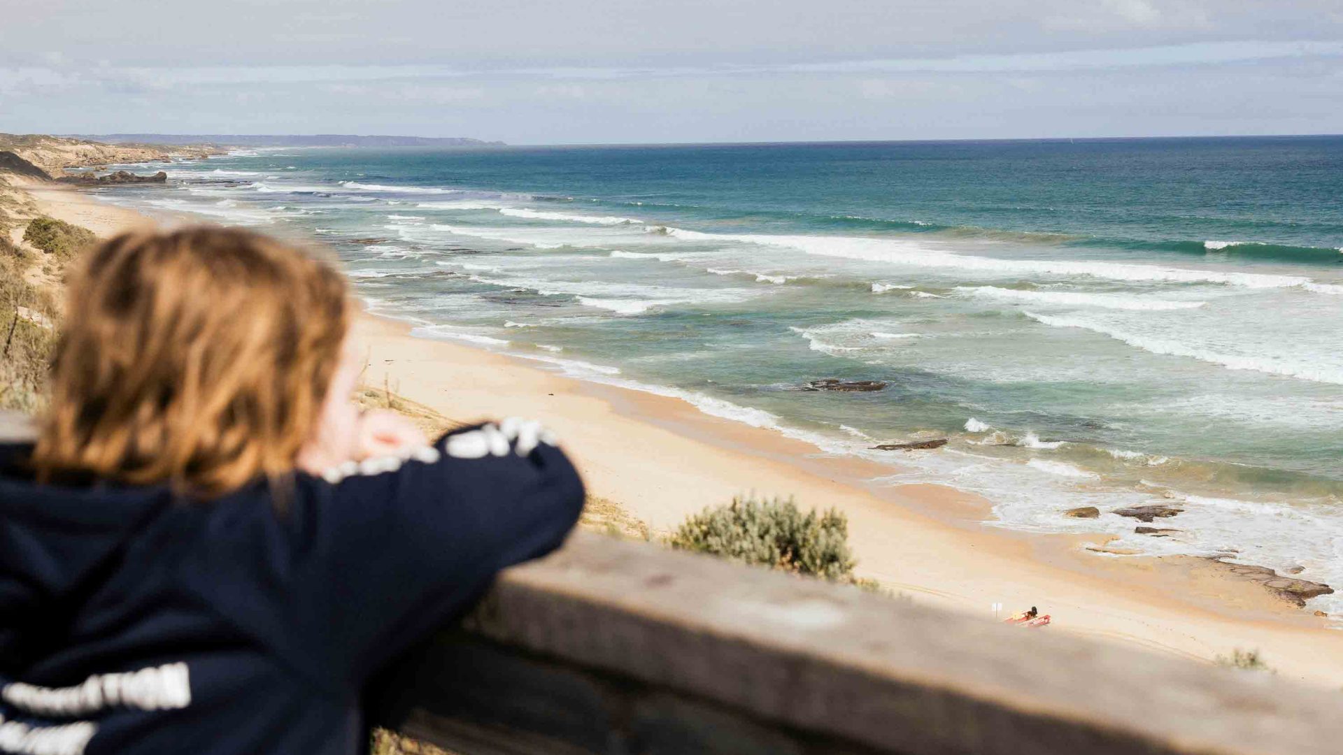 A young boy looks out at the surf from a lookout.