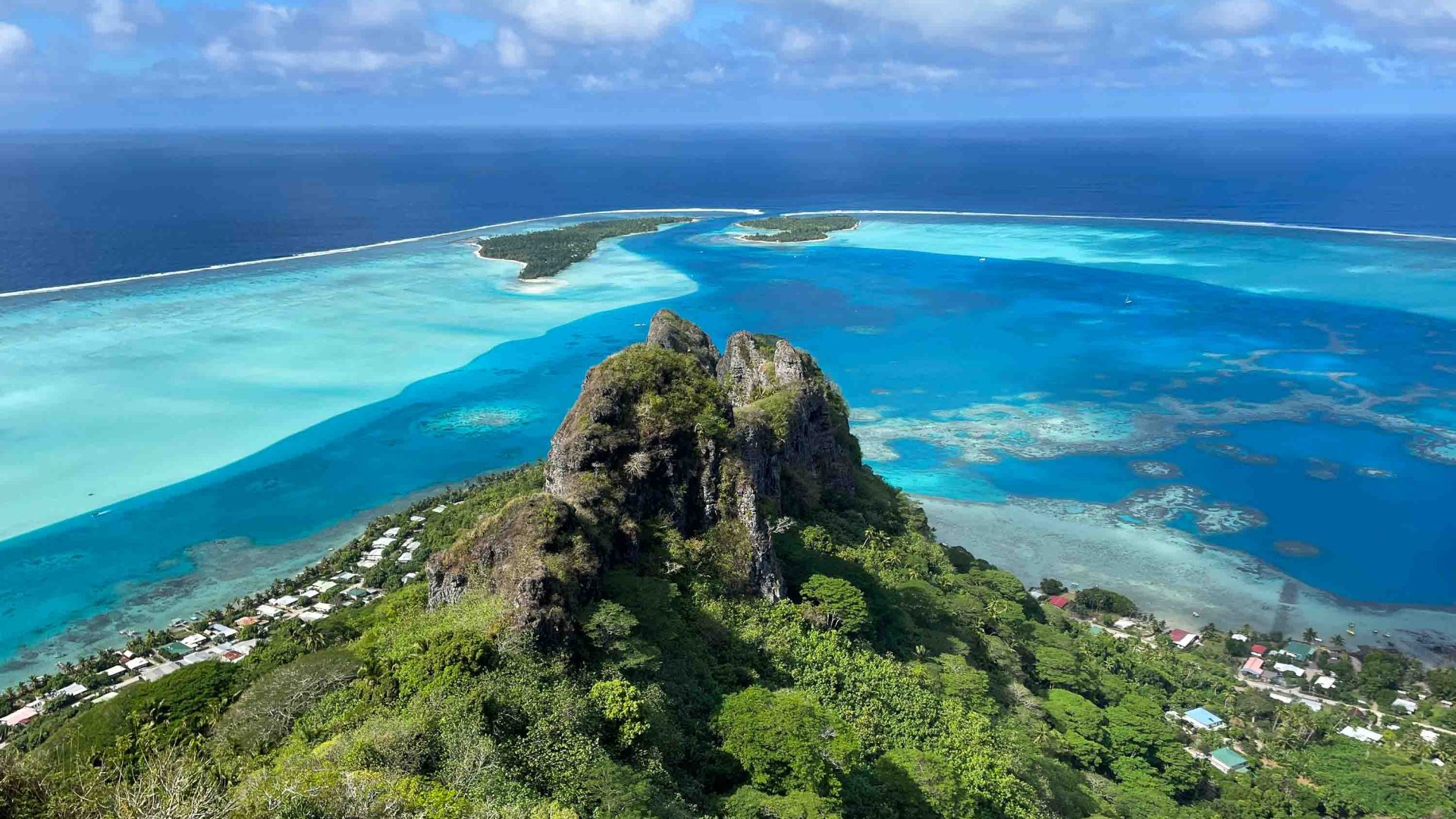 A mountain rises out of forest overlooking turquoise water.