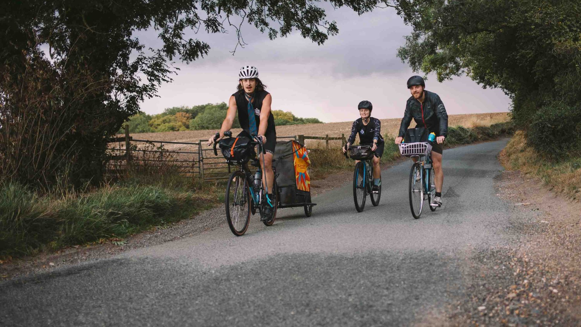 Three people ride along a dirt road fringed with trees.