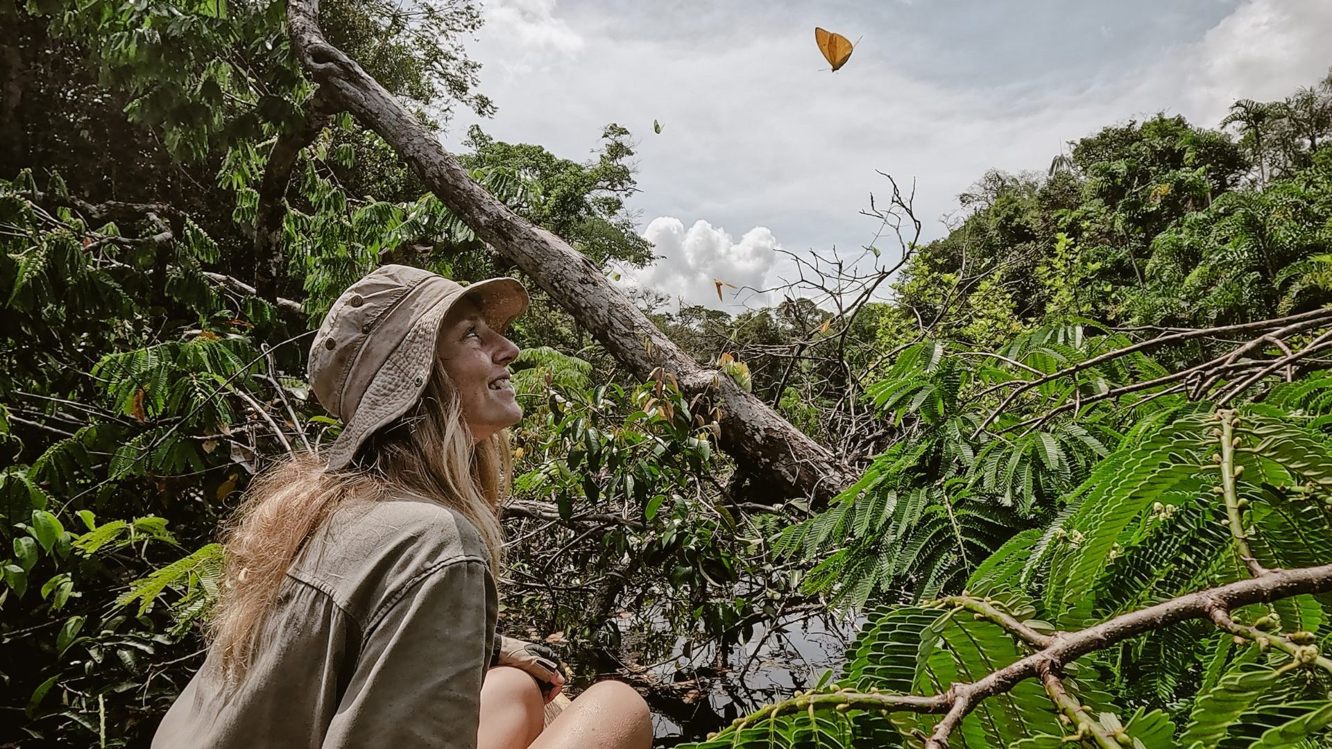 Woman smiles at orange butterfly above her head.