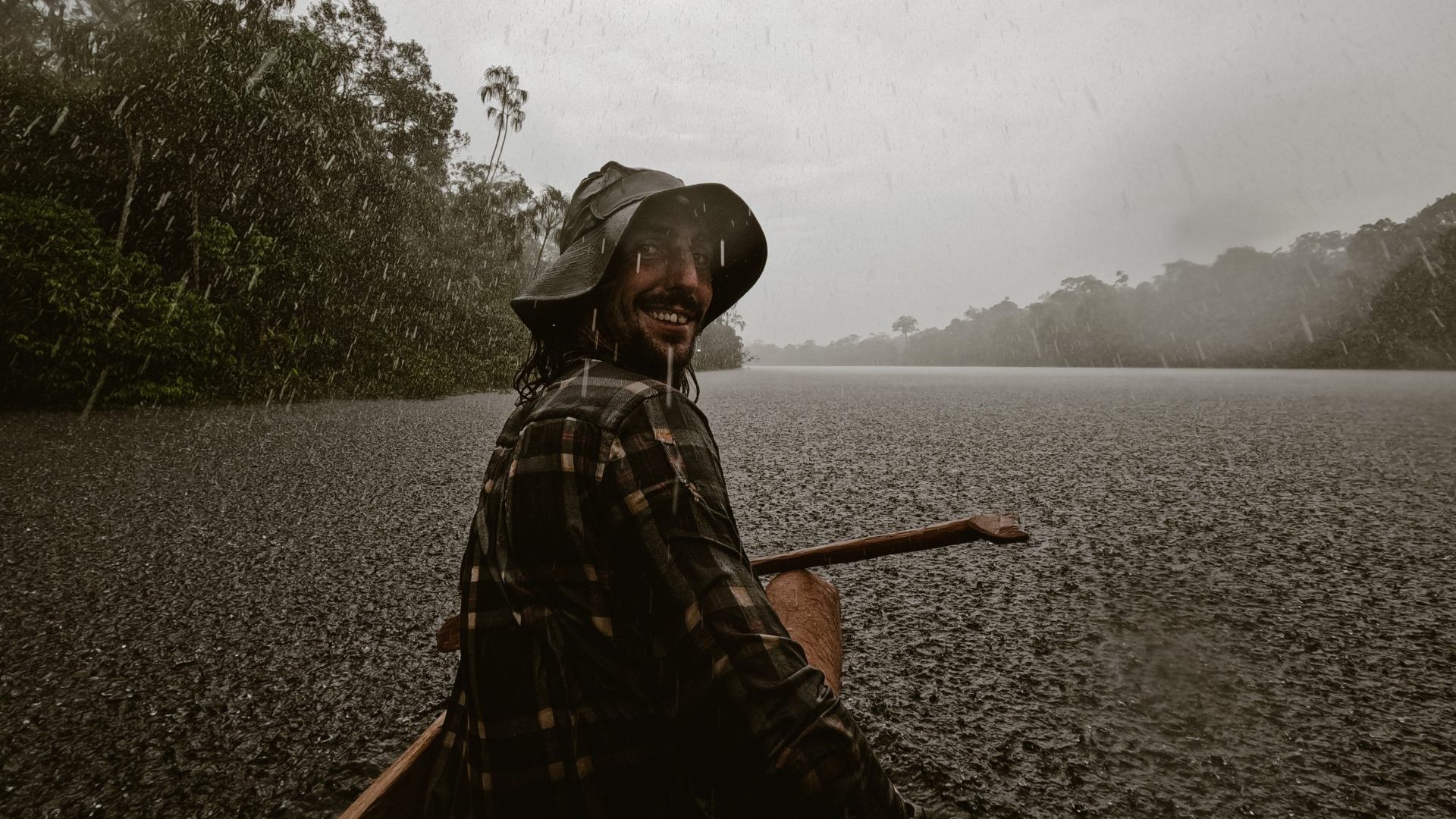 Man smiles at camera while paddling canoe in the rain