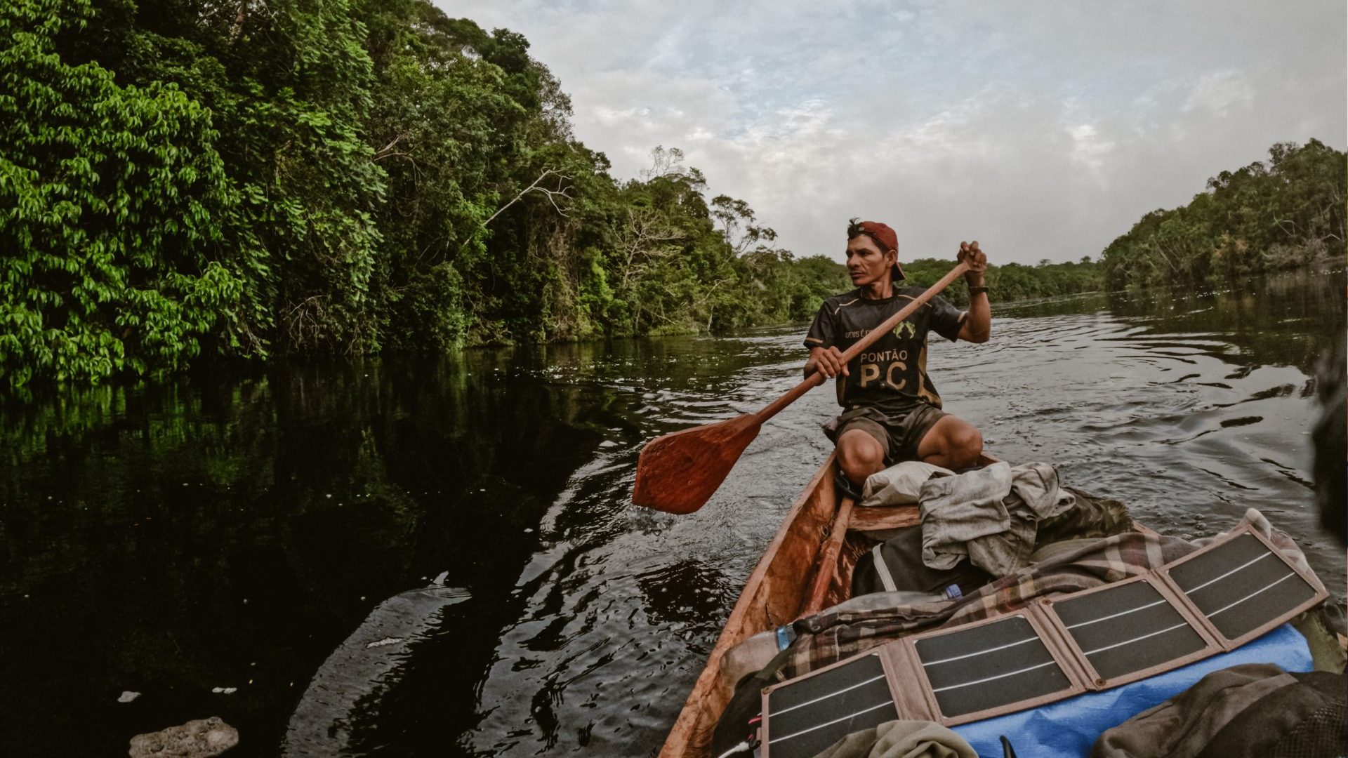 A man paddles down river with a canoe filled with solar panels and backpacks.