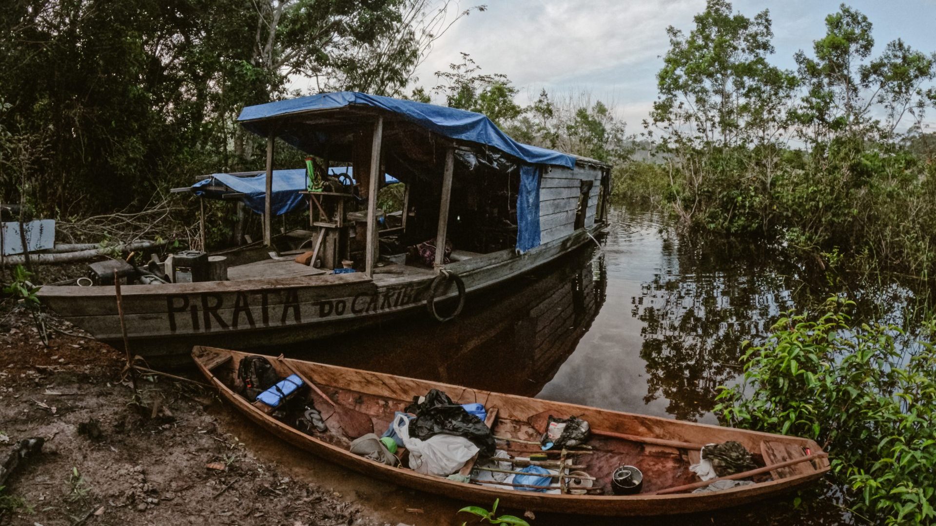 A larger boat next to dugout canoe on the bank of Amazon river