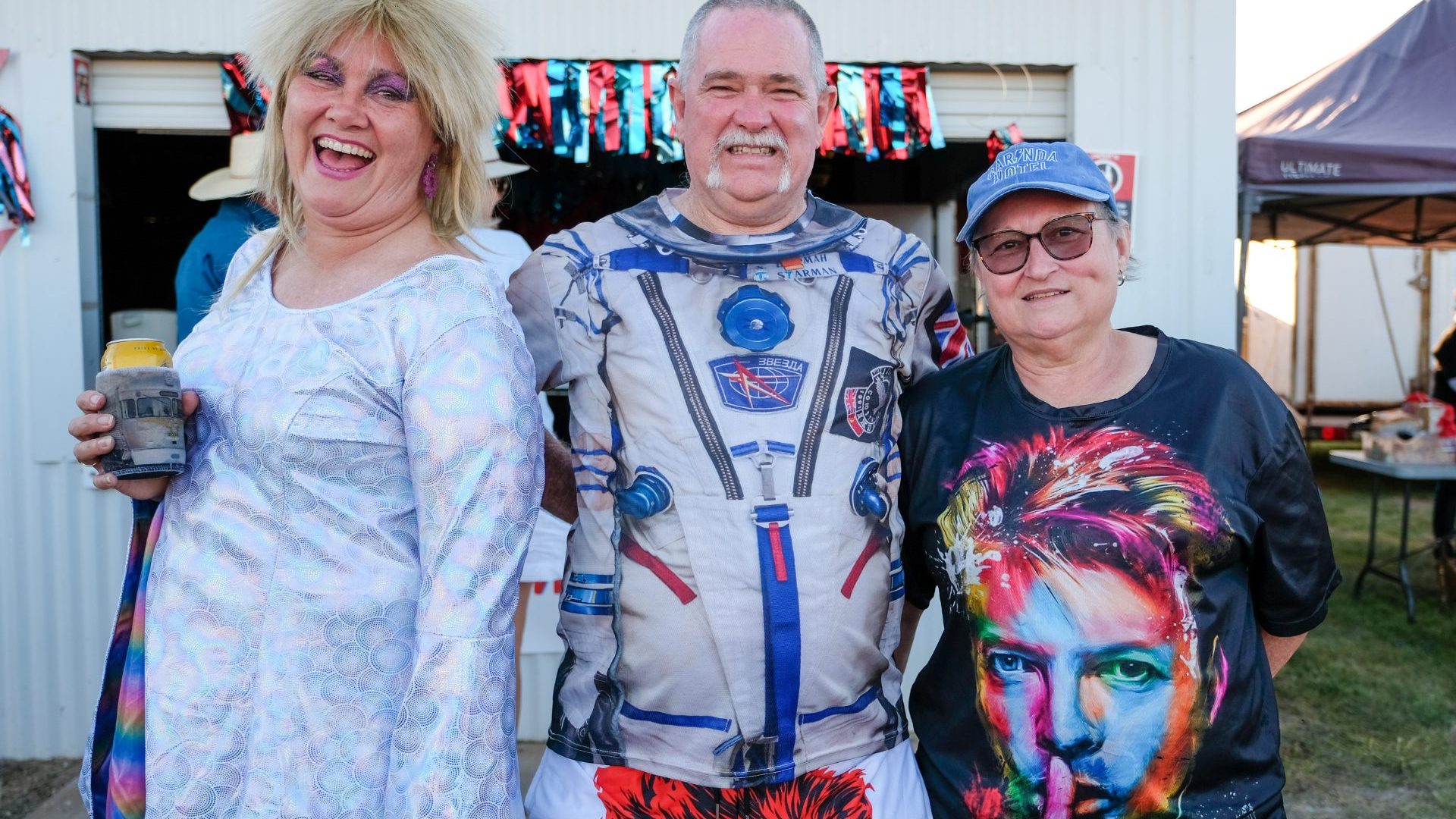 Three people dressed in David Bowie costumes smile.