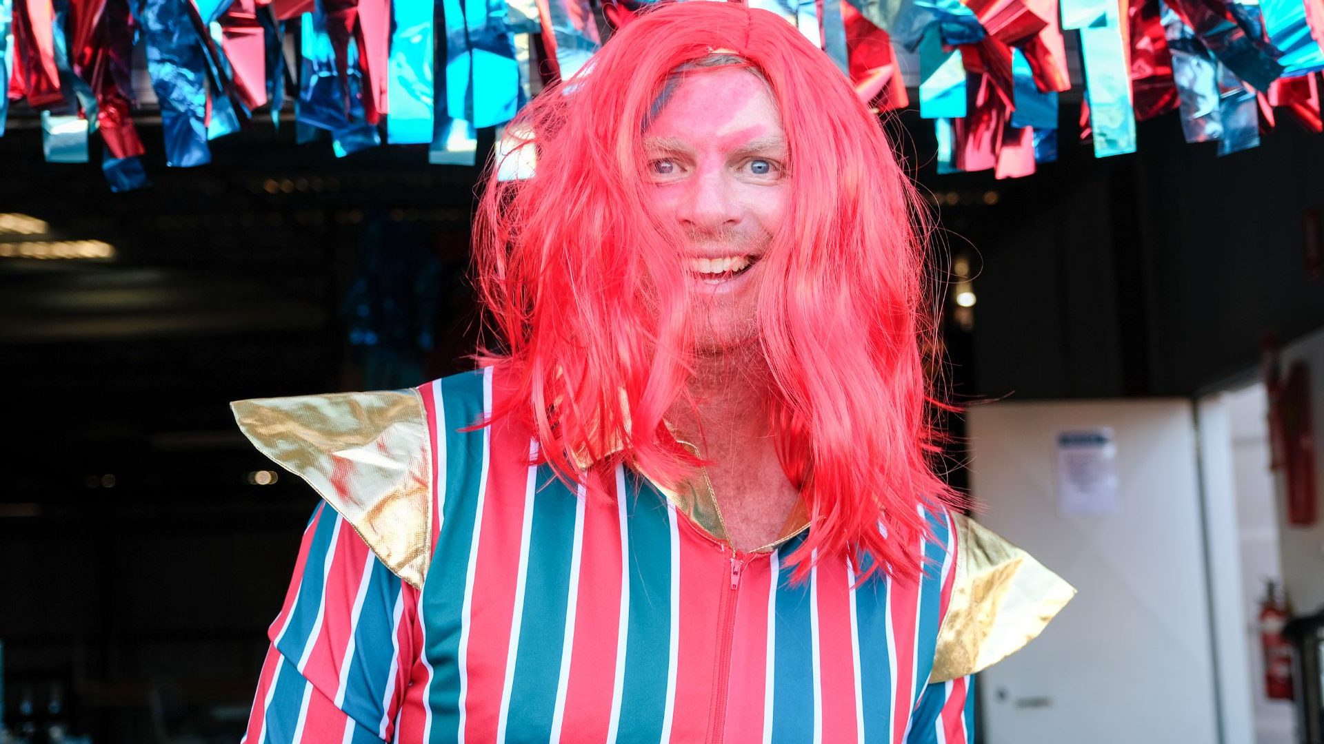 Man wearing red wig and striped jumpsuit.