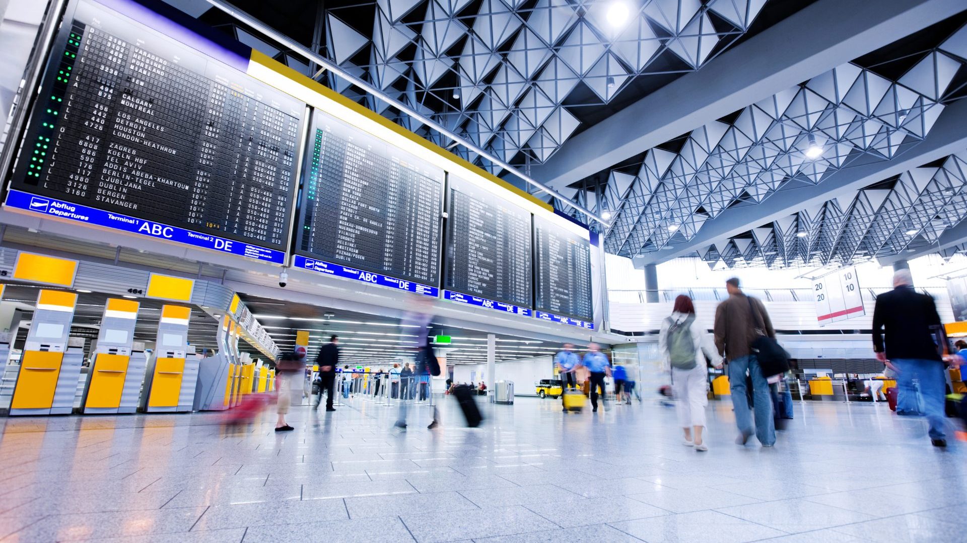 Airport flight board lit up under white lights.