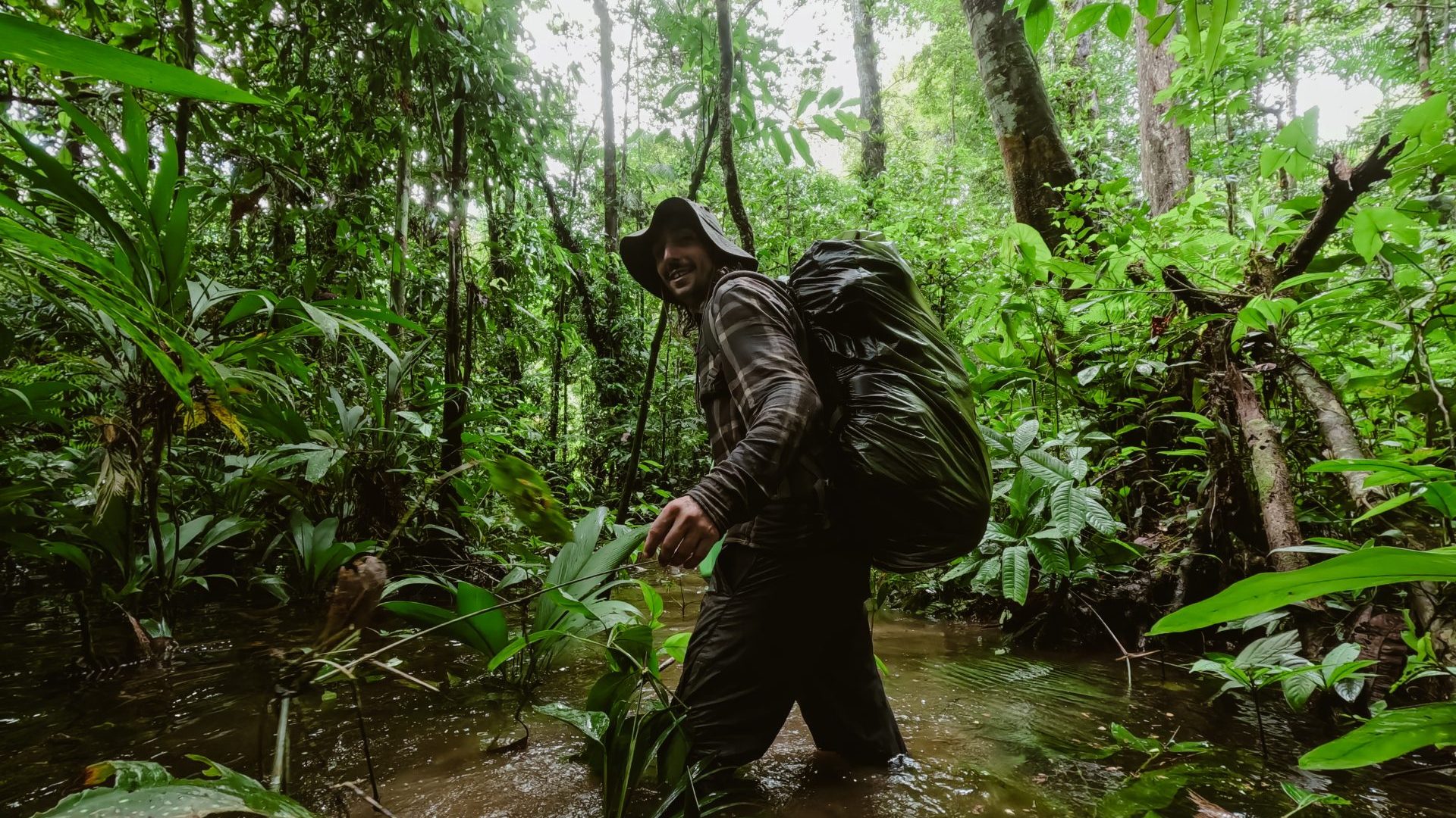 Man walks through knee deep water in green jungle.