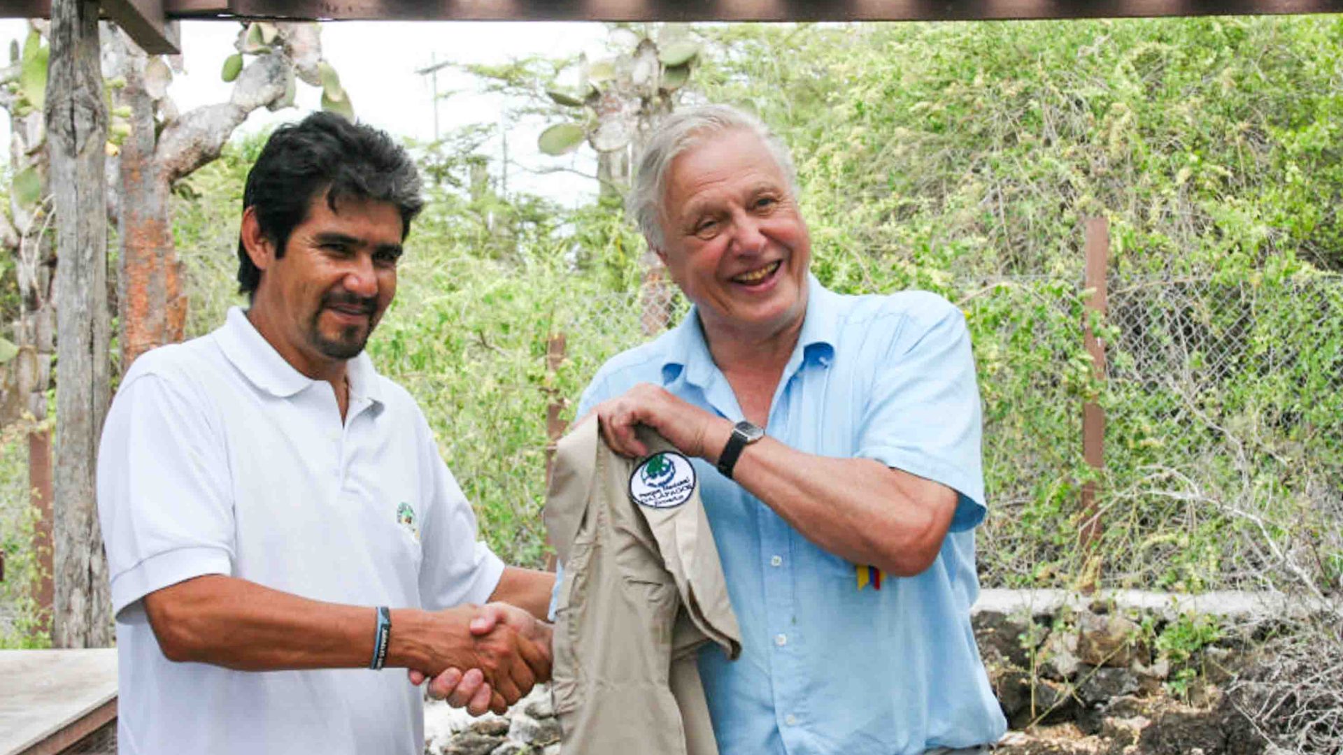 Two men shake hands while a shirt is held up.