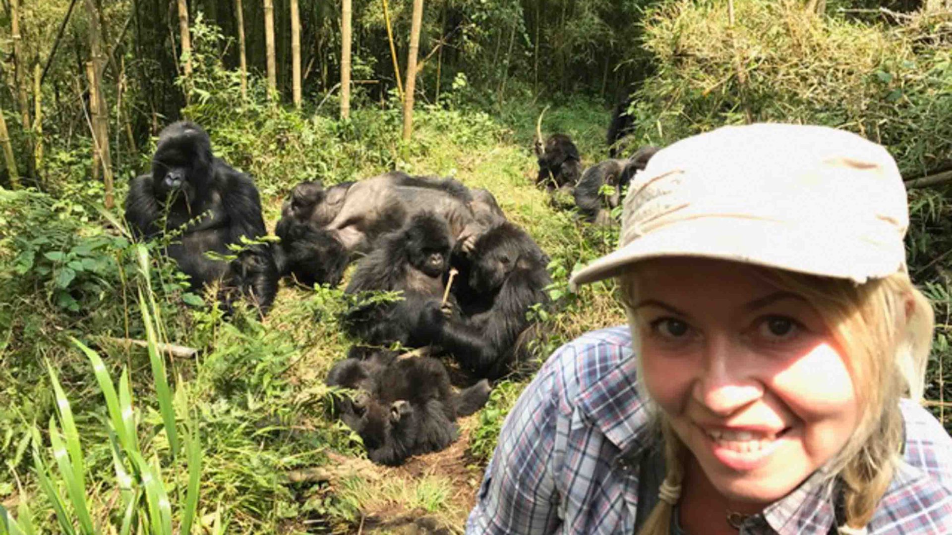 A woman smiles in the foreground. Gorillas are in the background behind her.