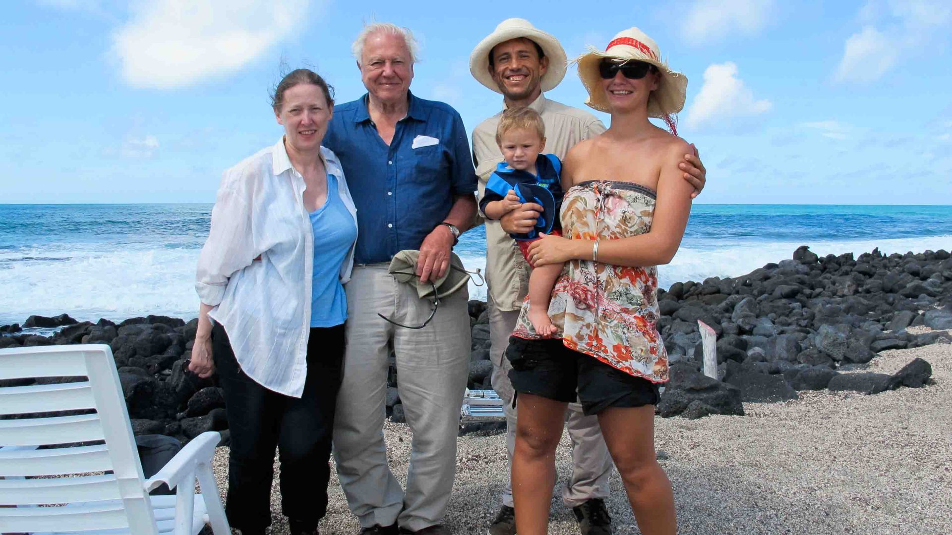 A group of people smile for a portrait on a beach.