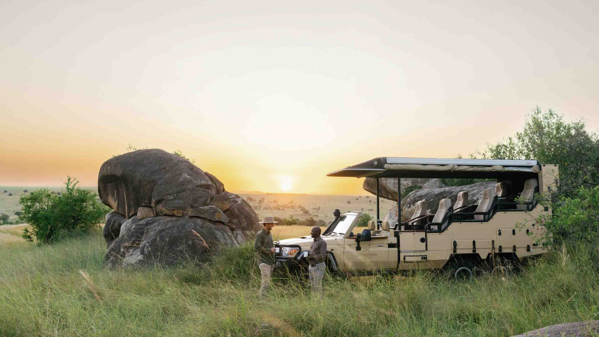 A guide speaks with a tourist while standing my a safari vehicle.
