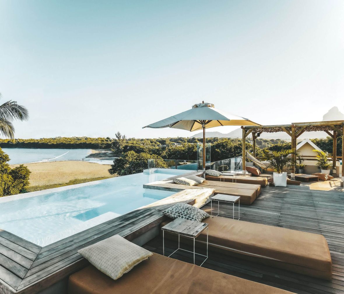 A hotel pool looking over a beach with calm water.
